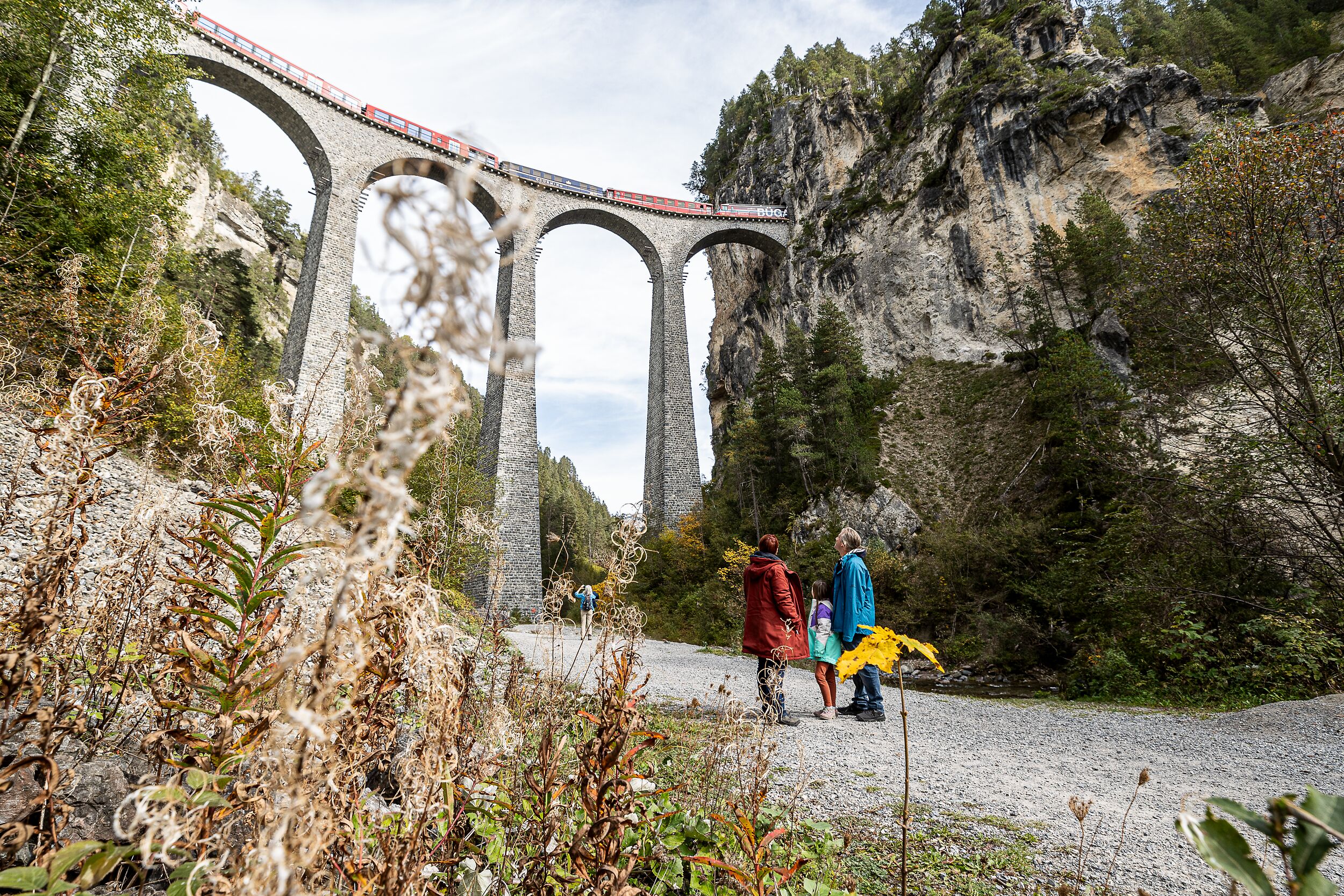 Eine Familie steht auf dem Viaduktplatz und schaut von unten auf den Landwasserviadukt. 