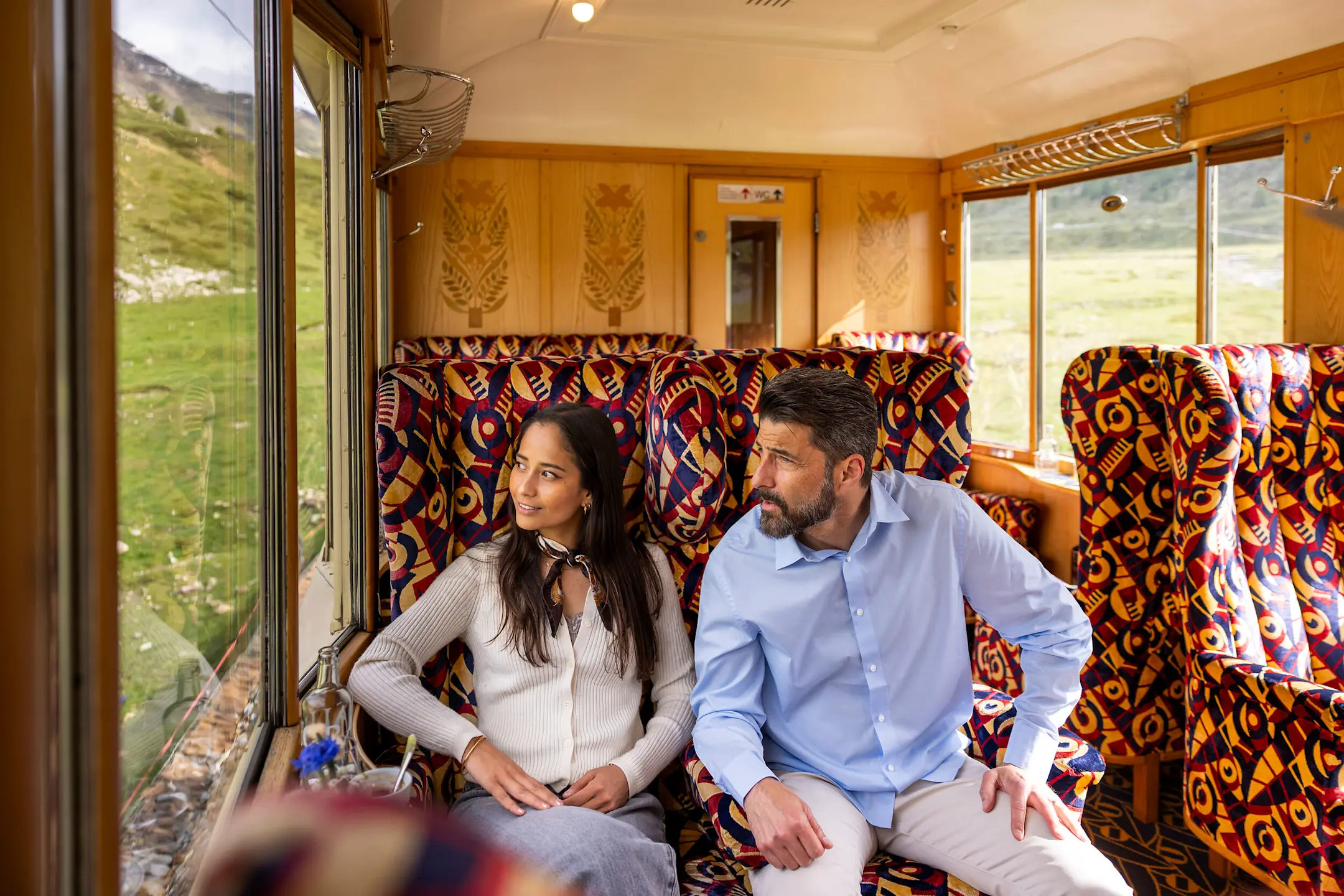 Zwei Personen sitzen im Pullman-Wagen und schauen durch die Fenster nach draussen.