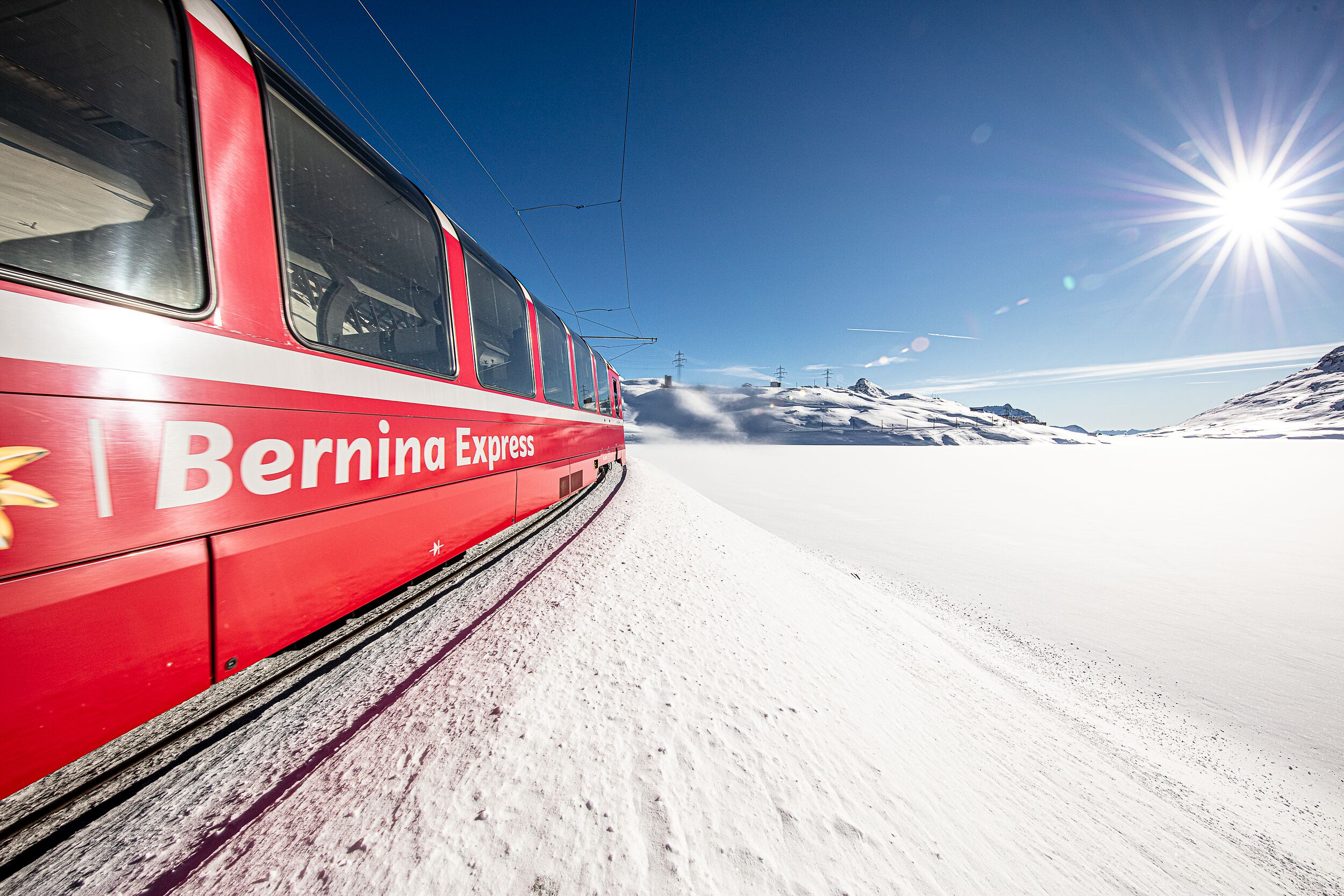 The red Bernina Express train travels along the snow-covered Lago Bianco.