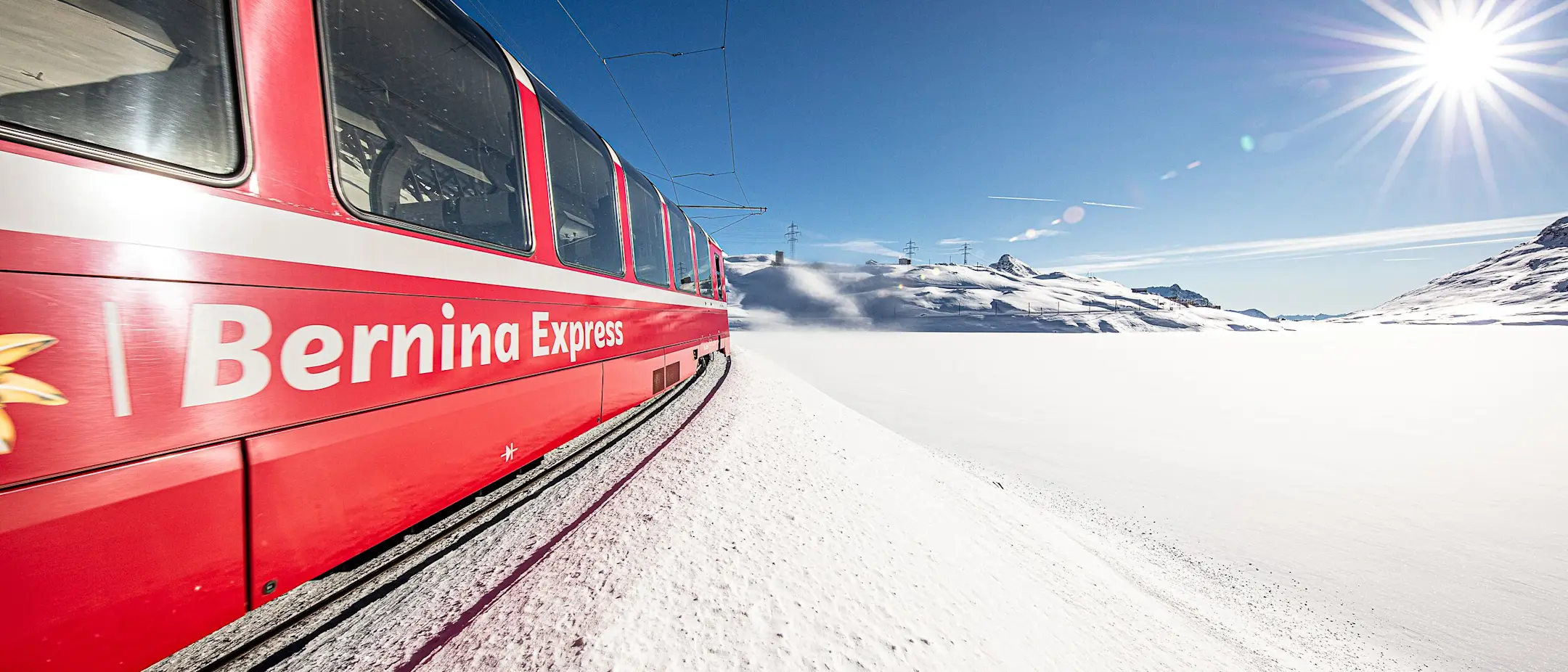 The red Bernina Express train travels along the snow-covered Lago Bianco.