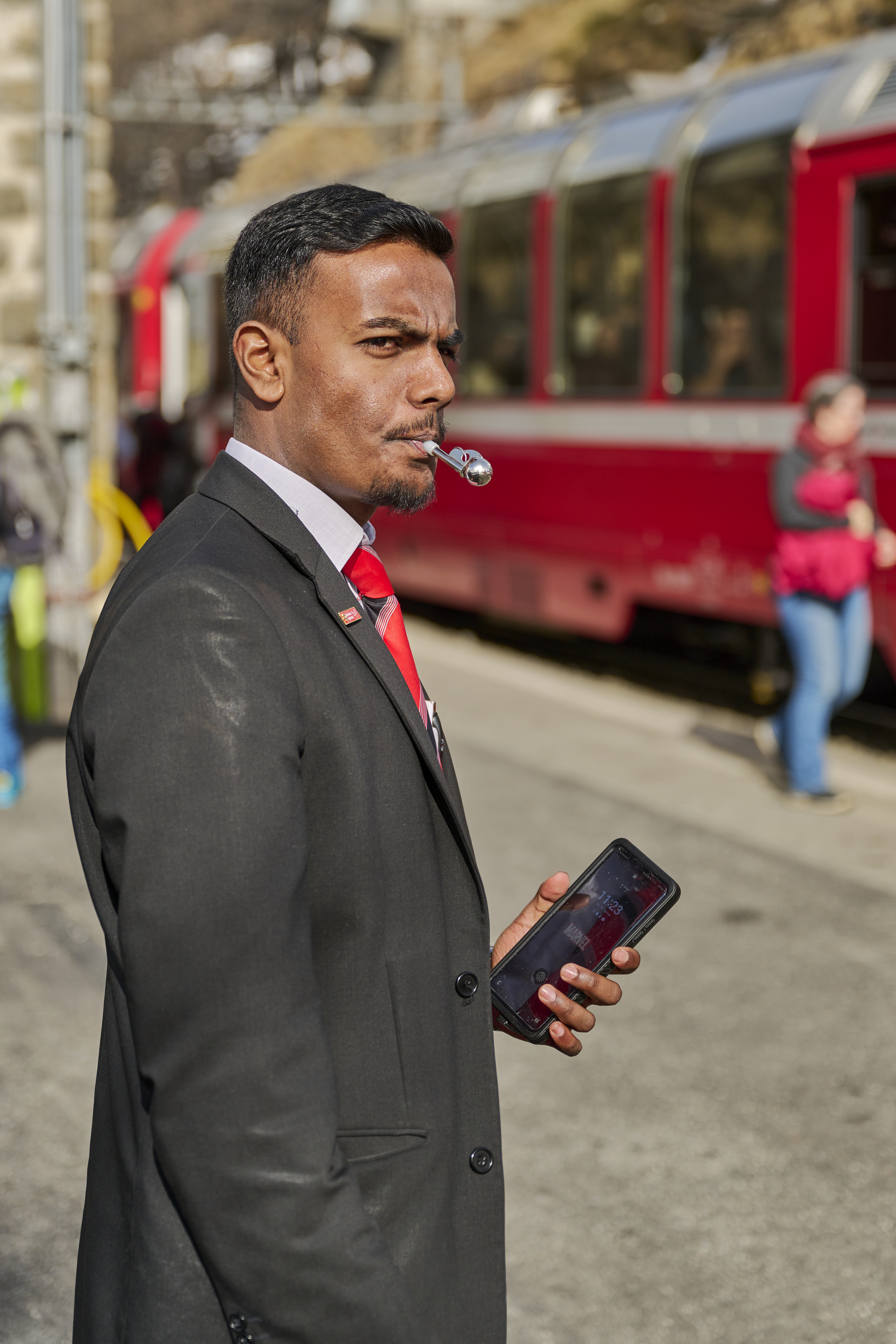 Ein zugbegleiter der RhB signalisiert mit seiner Pfeife die Abfahrt des Zuges. 