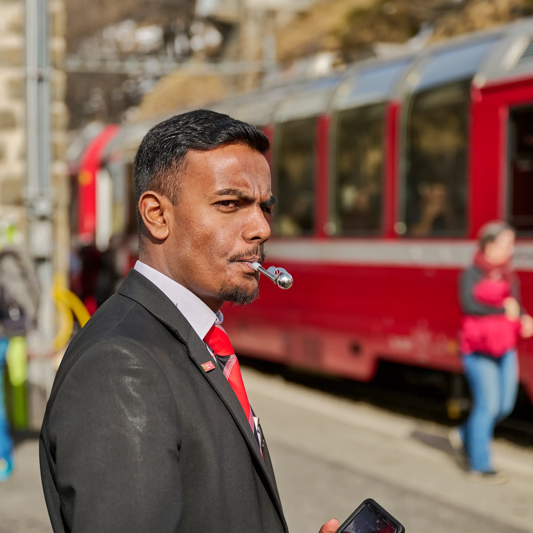 Ein zugbegleiter der RhB signalisiert mit seiner Pfeife die Abfahrt des Zuges.