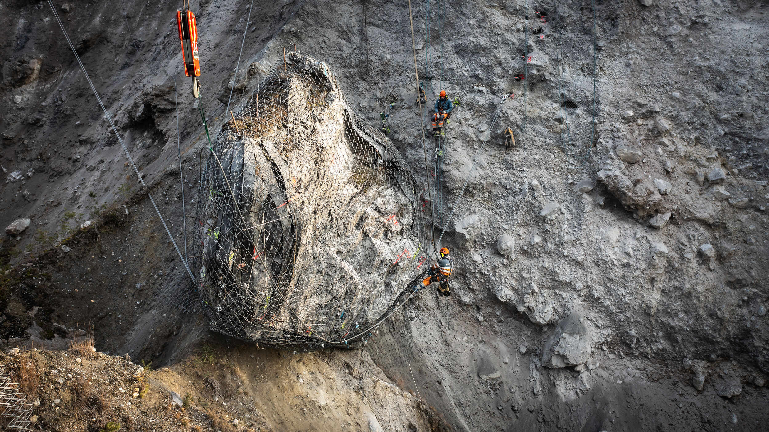 Ein riesiger Felsblock wird in der Rheinschlucht mit Drahtseilen am Berg gesichert.