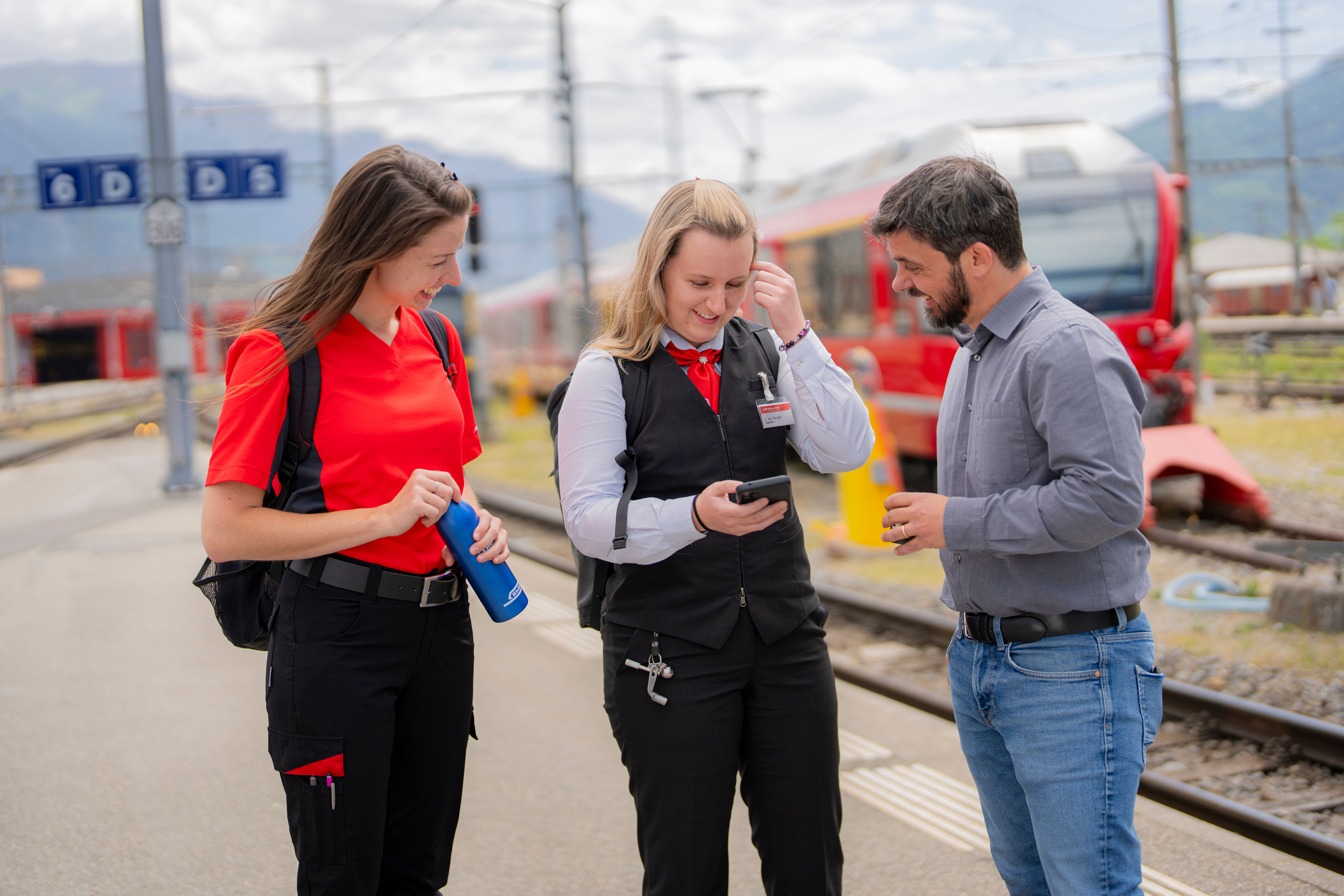 Zugbegleiter Lokführerin und Bürolist mit Mobiltelefon etwas am Besprechen auf Perron