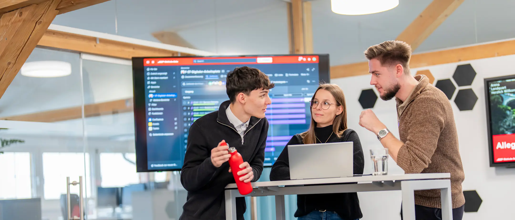 Zwei Mitarbeiter und eine Mitarbeiterin bei Besprechung vor einem Screen an einem Stehtisch