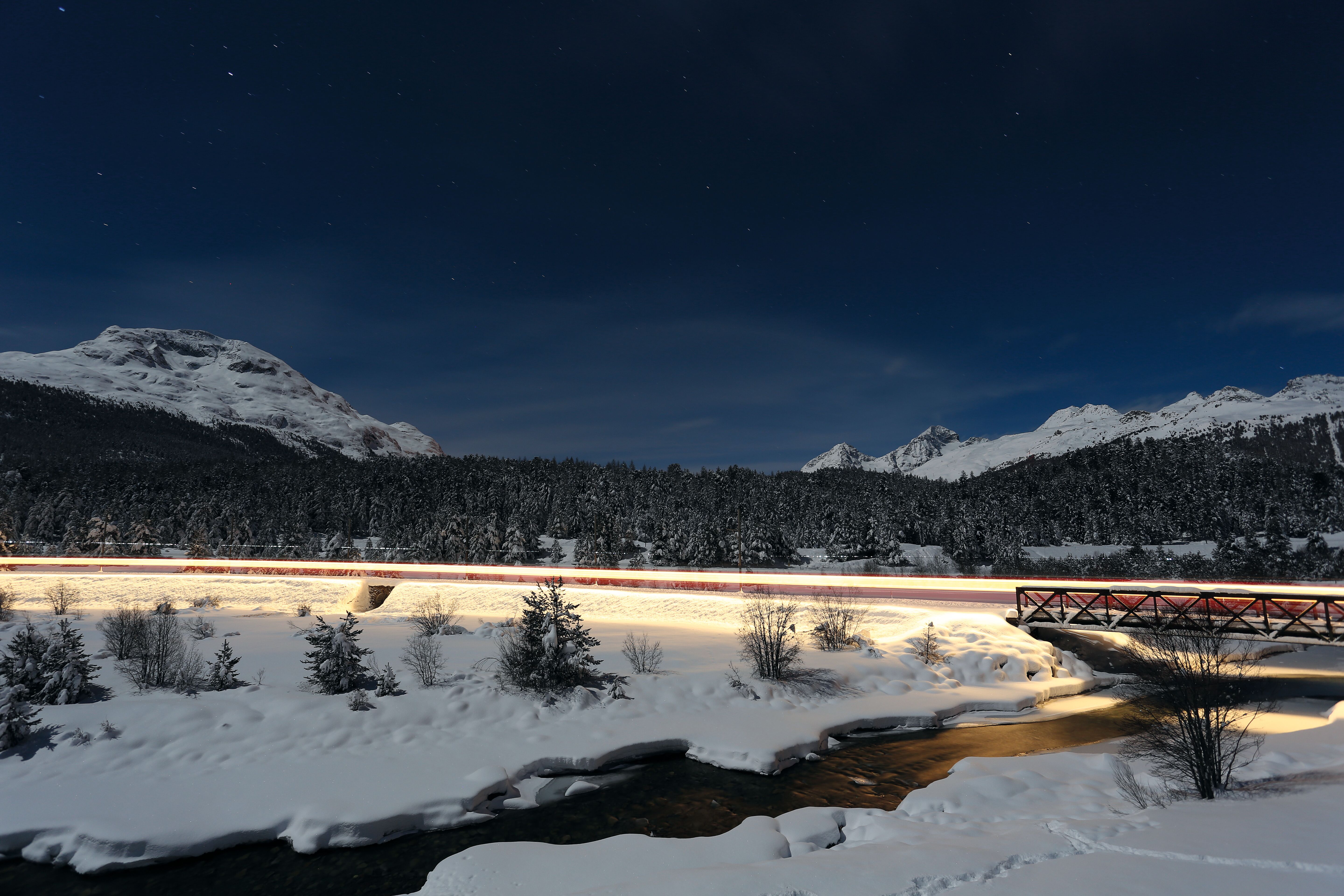 Langzeitbelichtung eines beleuchteten Zuges, der sich bei Nacht durch die verschneite Landschaft schlängelt. 