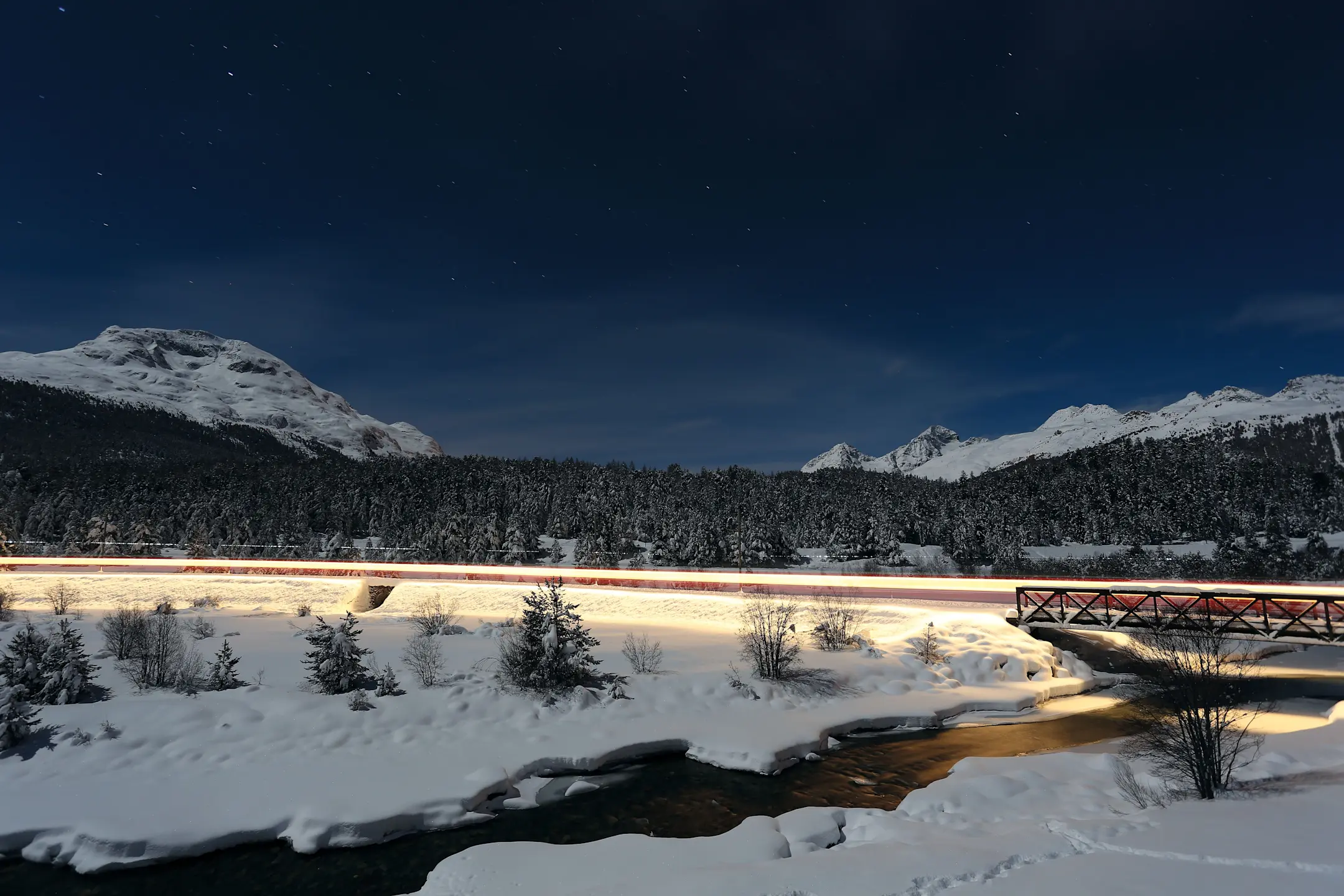 Langzeitbelichtung eines beleuchteten Zuges, der sich bei Nacht durch die verschneite Landschaft schlängelt.