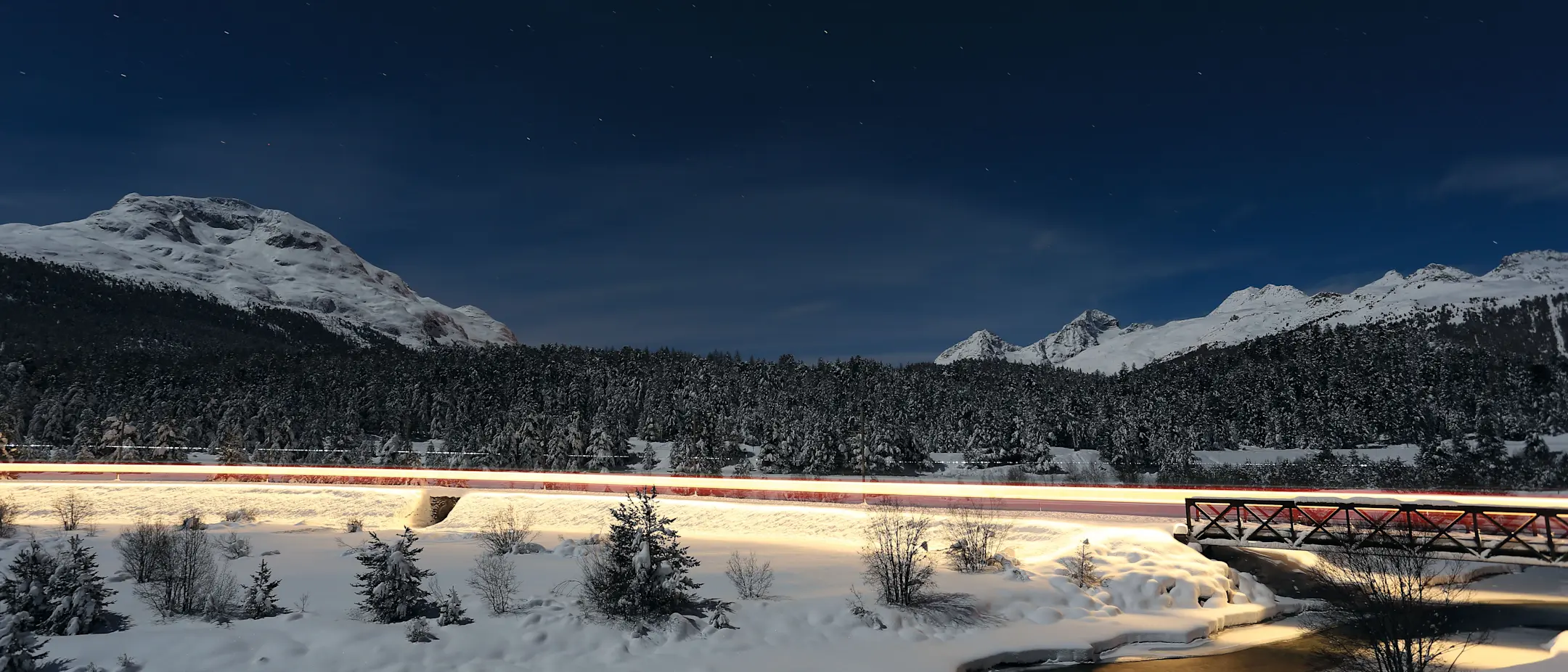 Langzeitbelichtung eines beleuchteten Zuges, der sich bei Nacht durch die verschneite Landschaft schlängelt.