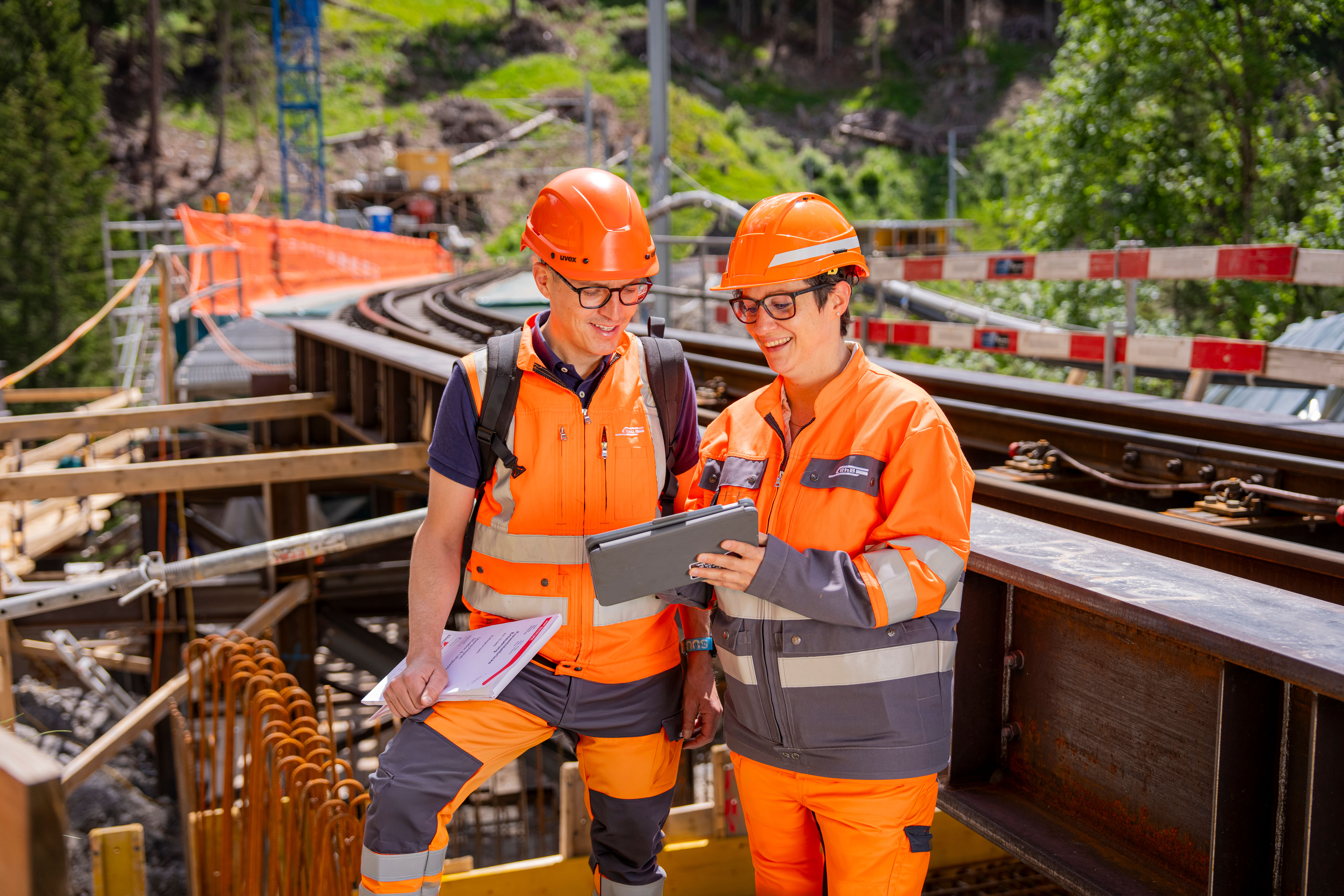 Zwei Bauarbeiter stehen vor einer Baustelle und besprechen etwas auf dem Tablet