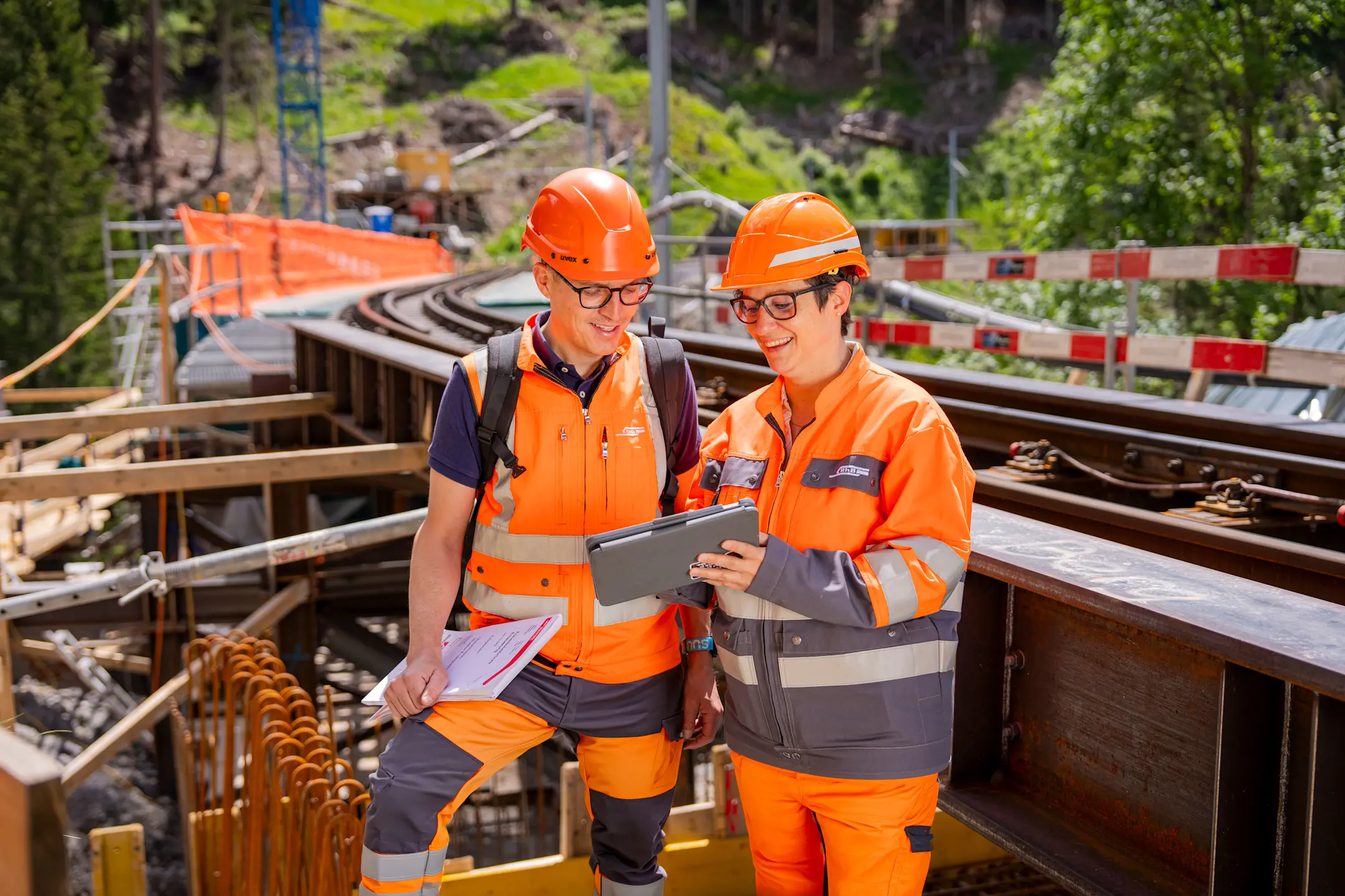 Zwei Bauarbeiter stehen vor einer Baustelle und besprechen etwas auf dem Tablet