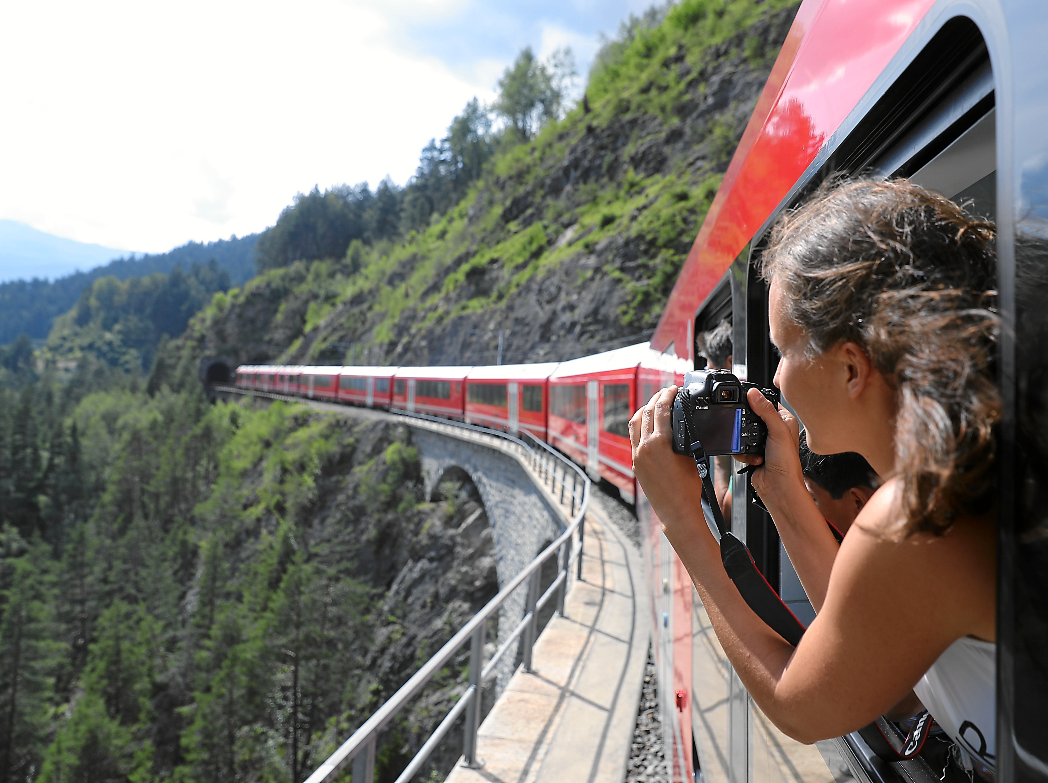 Eine Reisende hält eine Kamera aus einem Zug der Rhätischen Bahn
