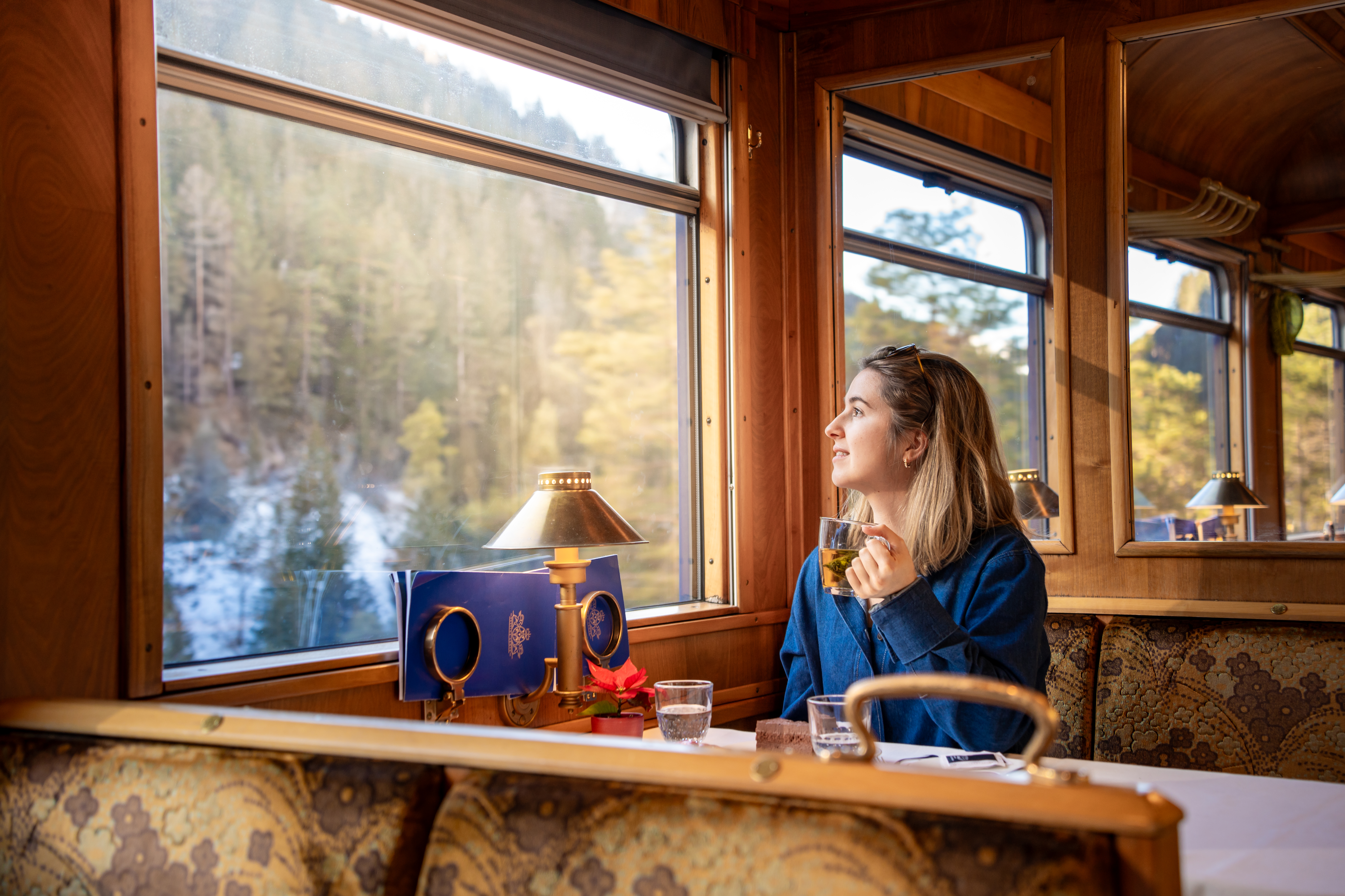 A woman in the historical RhB Gourmino dining car looks out of the window, holding a cup of tea.