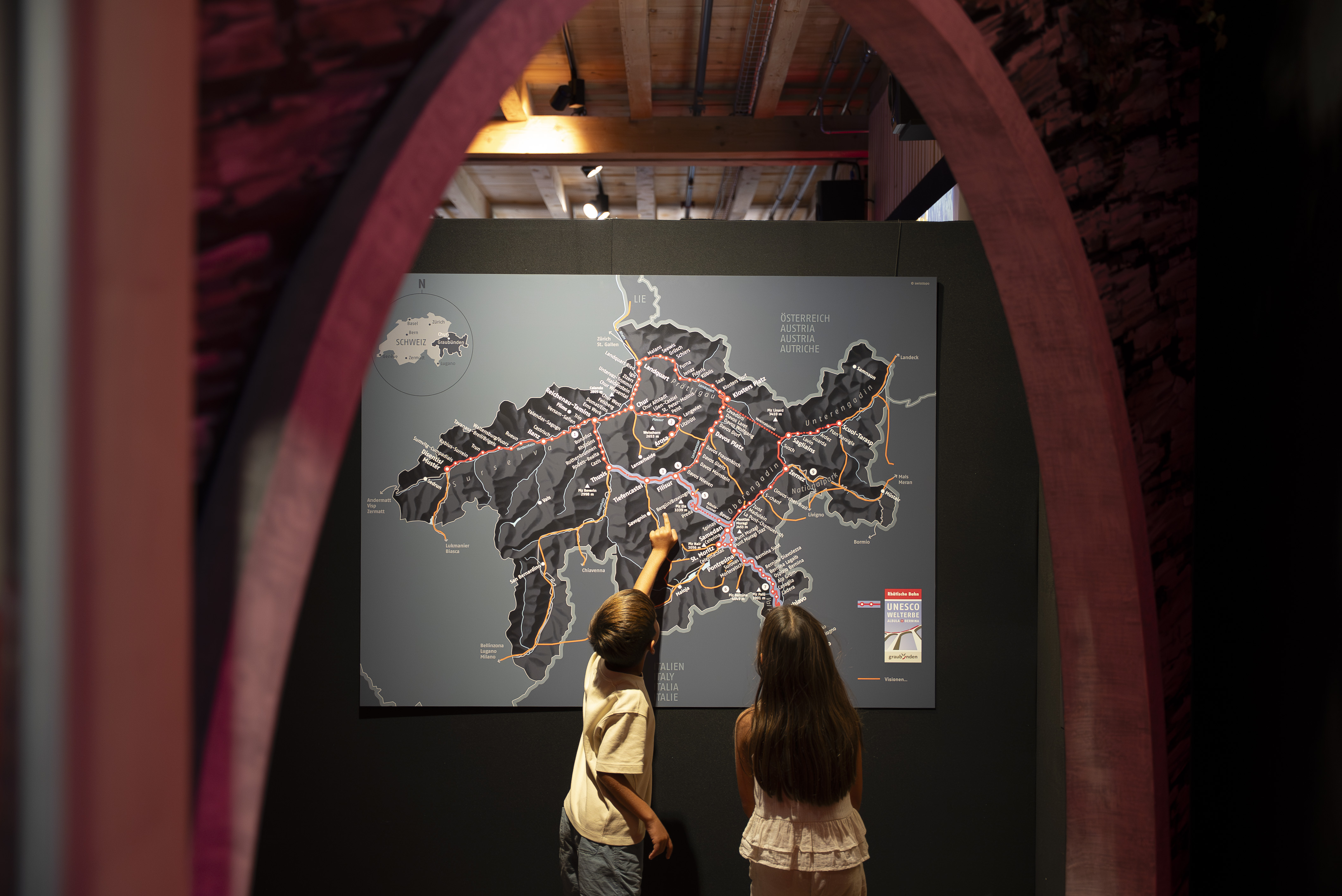 Zwei Kinder stehen im Bahnmuseum Albula staunend vor einer Karte Graubündens.