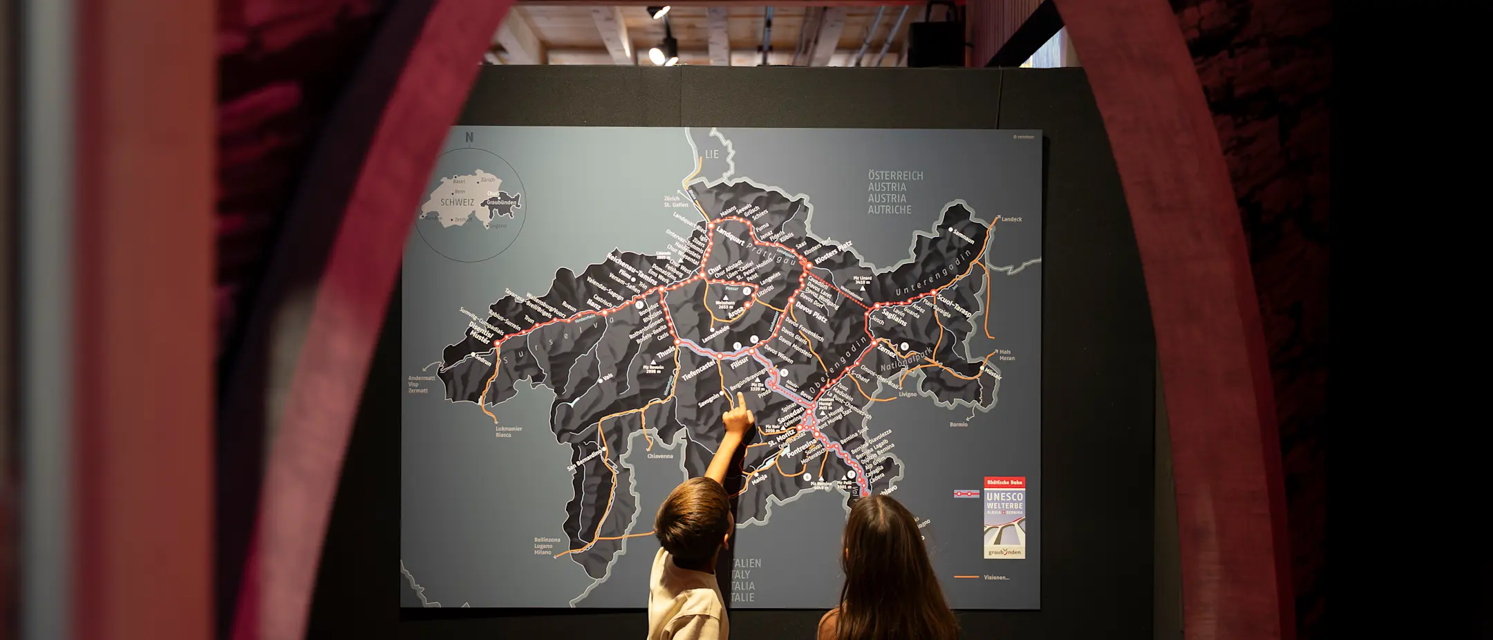 Zwei Kinder stehen im Bahnmuseum Albula staunend vor einer Karte Graubündens.