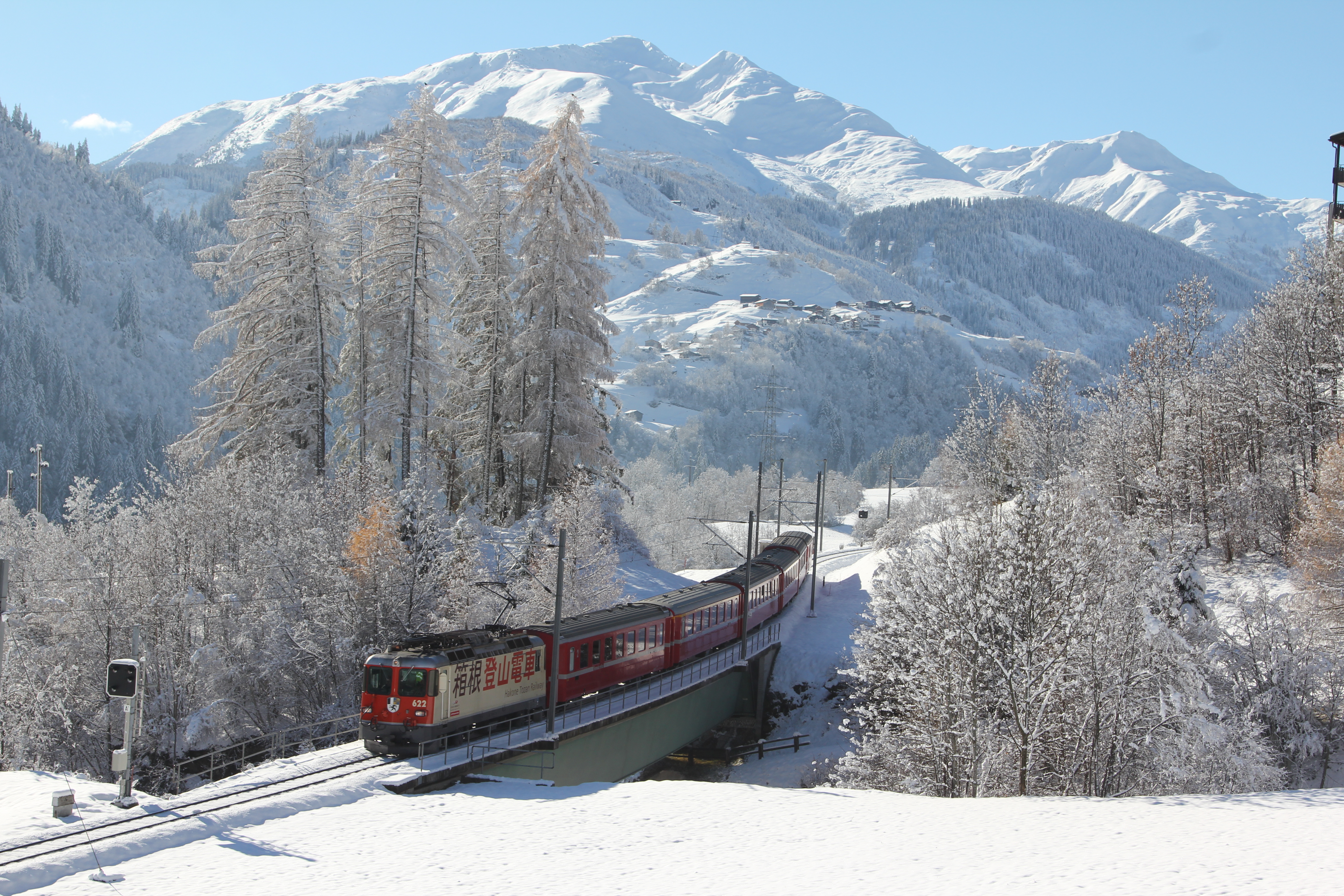A Regio Express train operated by the RhB travels through a snow-covered Alpine landscape near Disentis in winter.
