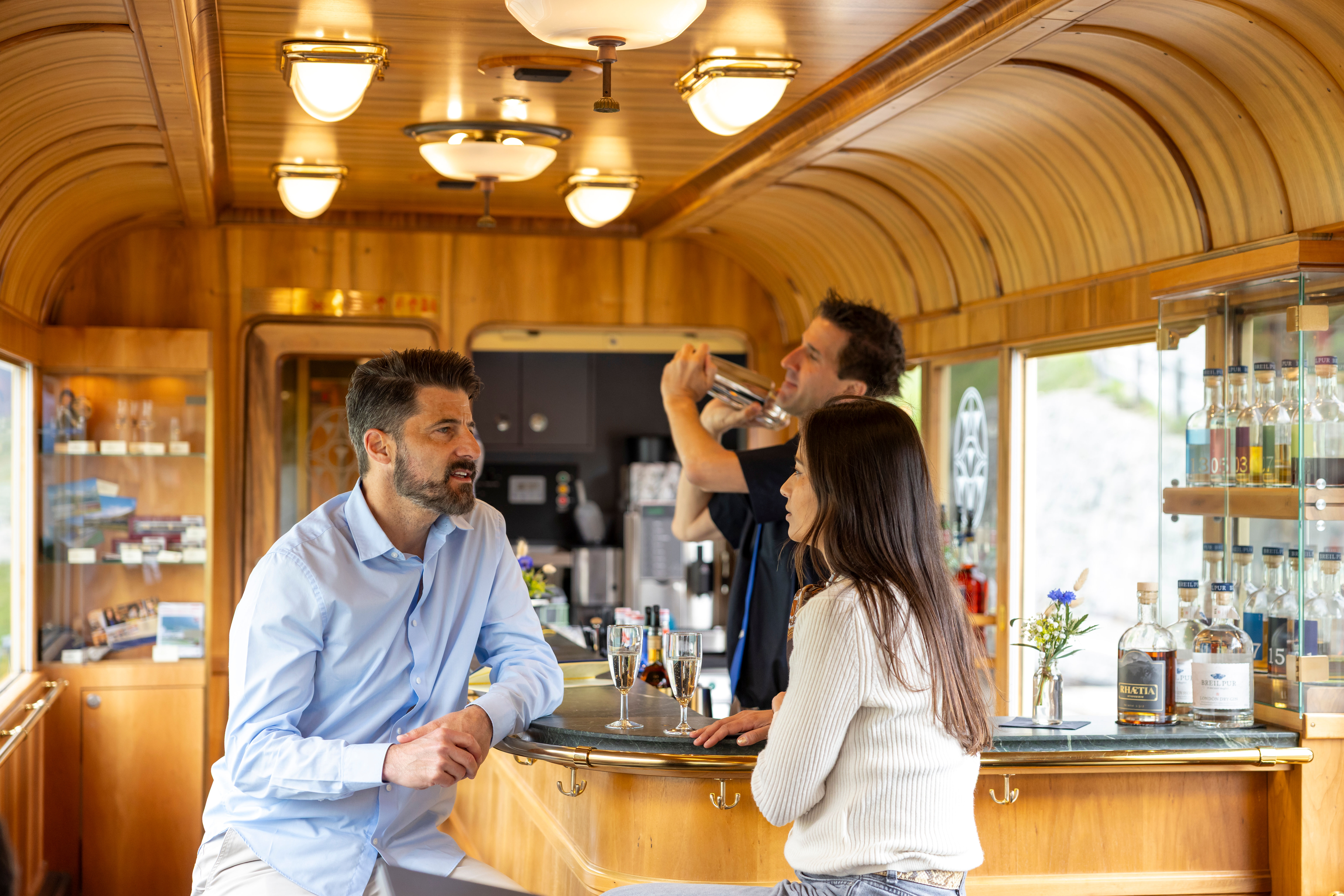 Zwei Menschen stossen mit Getränkegläsern an der Bar des Piano Bar Wagens an.