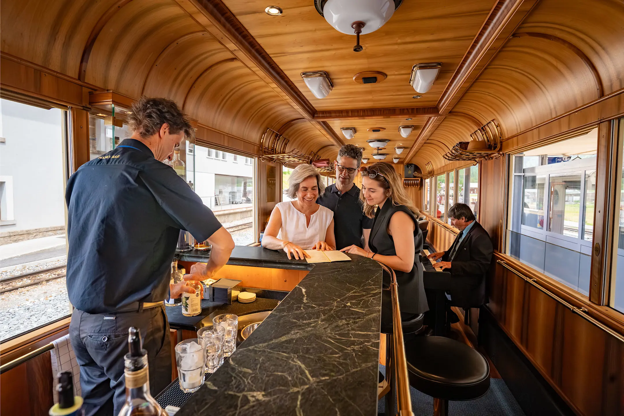 Drei Menschen stossen mit Getränkegläsern an der Bar des Piano Bar Wagens an.