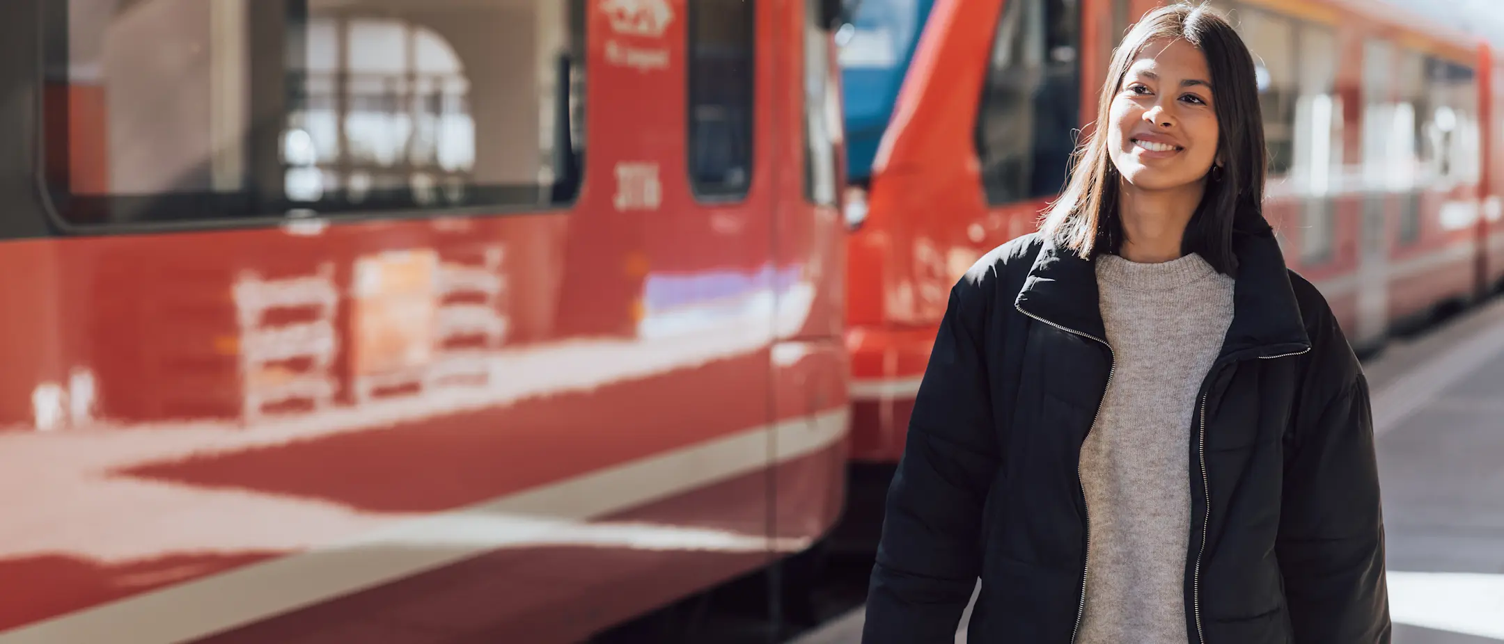 Junge Frau am Bahnsteig vor einem roten Zug der Rhätischen Bahn – bereit für die Reise durch Graubünden.