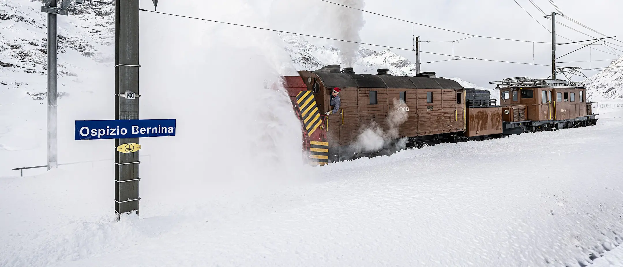 Dampfschneeschleuder der Rhätischen Bahn räumt verschneite Bahngleise auf dem Berninapass bei sonnigem Winterwetter frei.