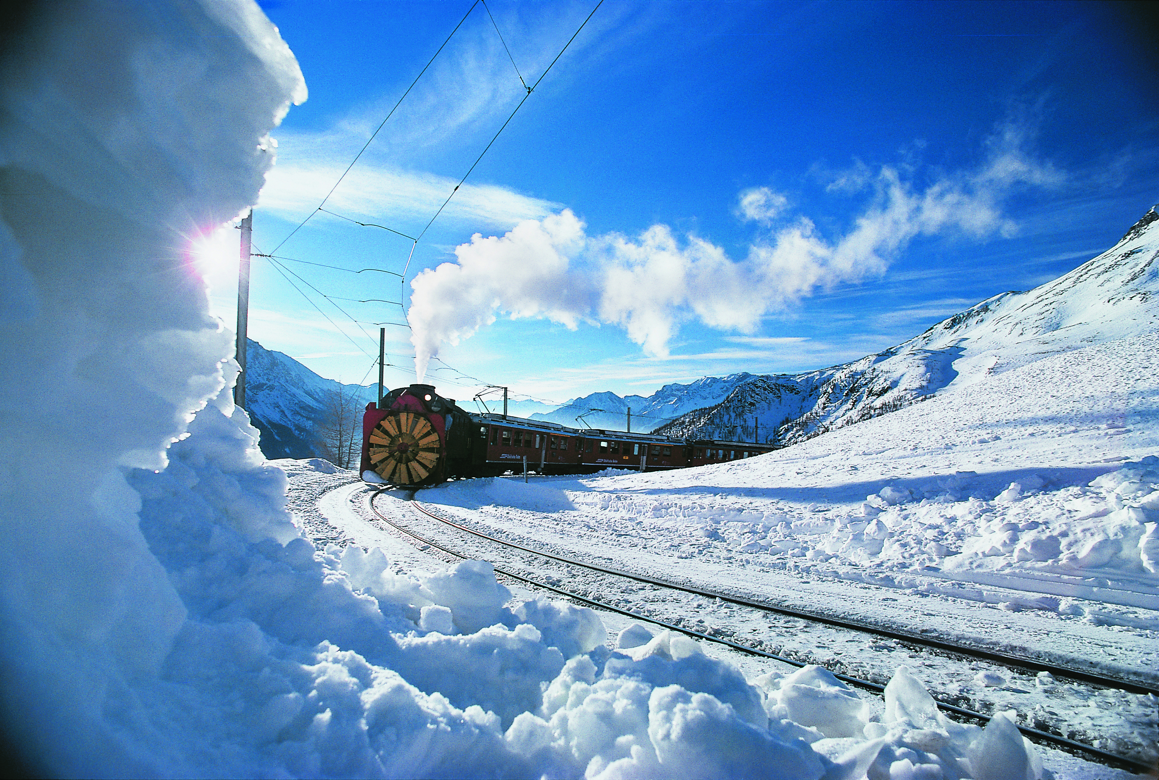 Dampfschneeschleuder der Rhätischen Bahn räumt verschneite Bahngleise auf dem Berninapass bei sonnigem Winterwetter frei.