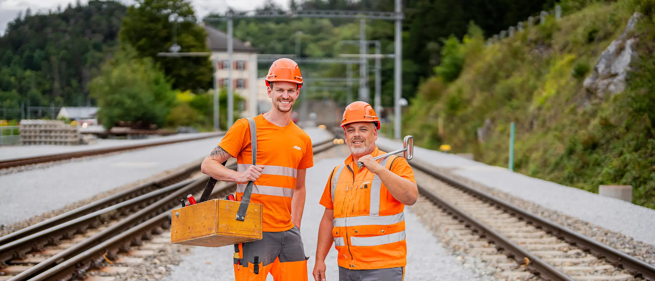 Zwei Elektroinstallateure mit Werkzeug präsentierten sich stolz zwischen zwei Gleisen.
