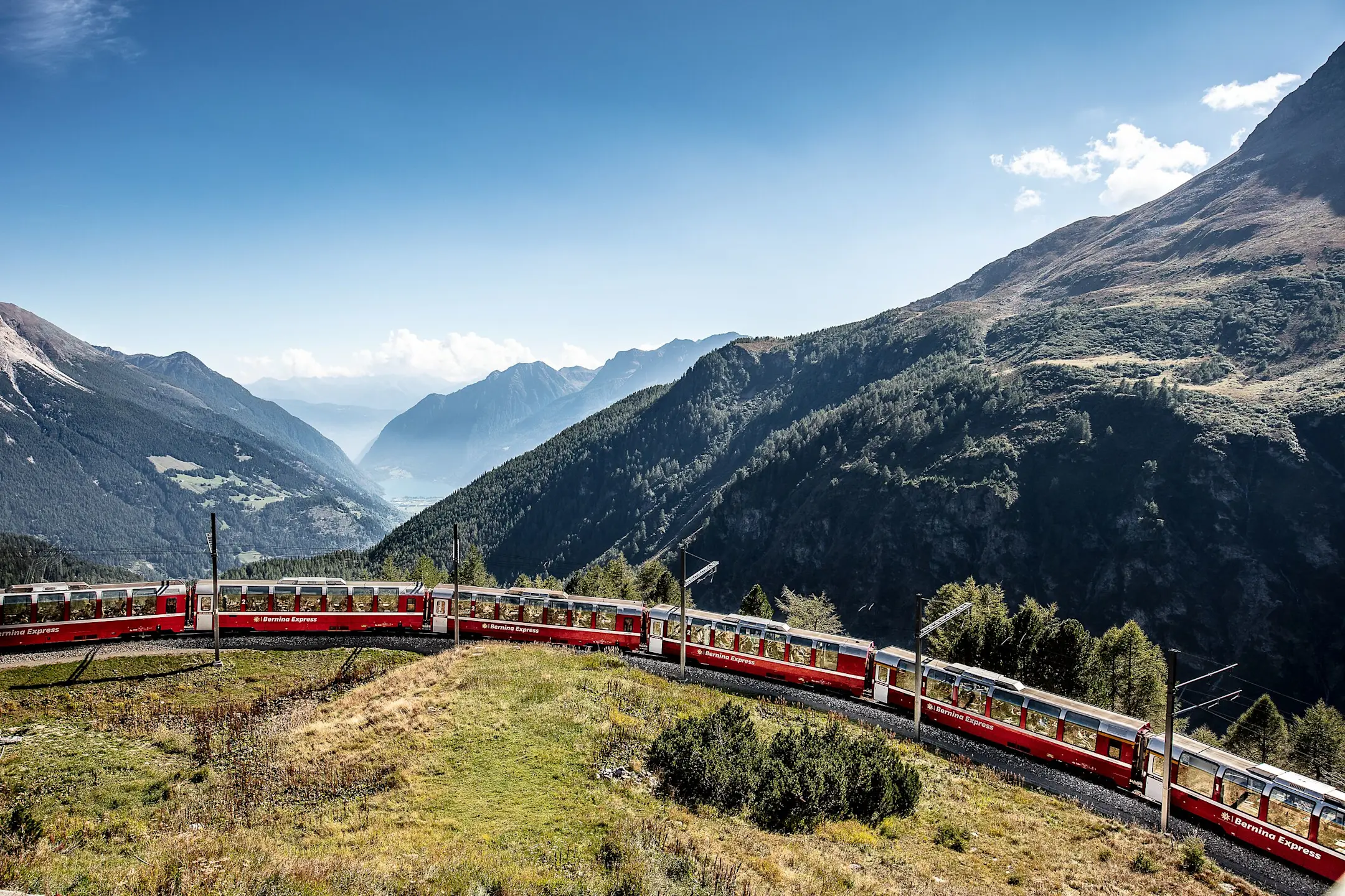 Der Bernina Express fährt bei der Alp Grüm eine Kurve. Im Hintergrund sieht man ins Tal Richtung Val Poschiavo.