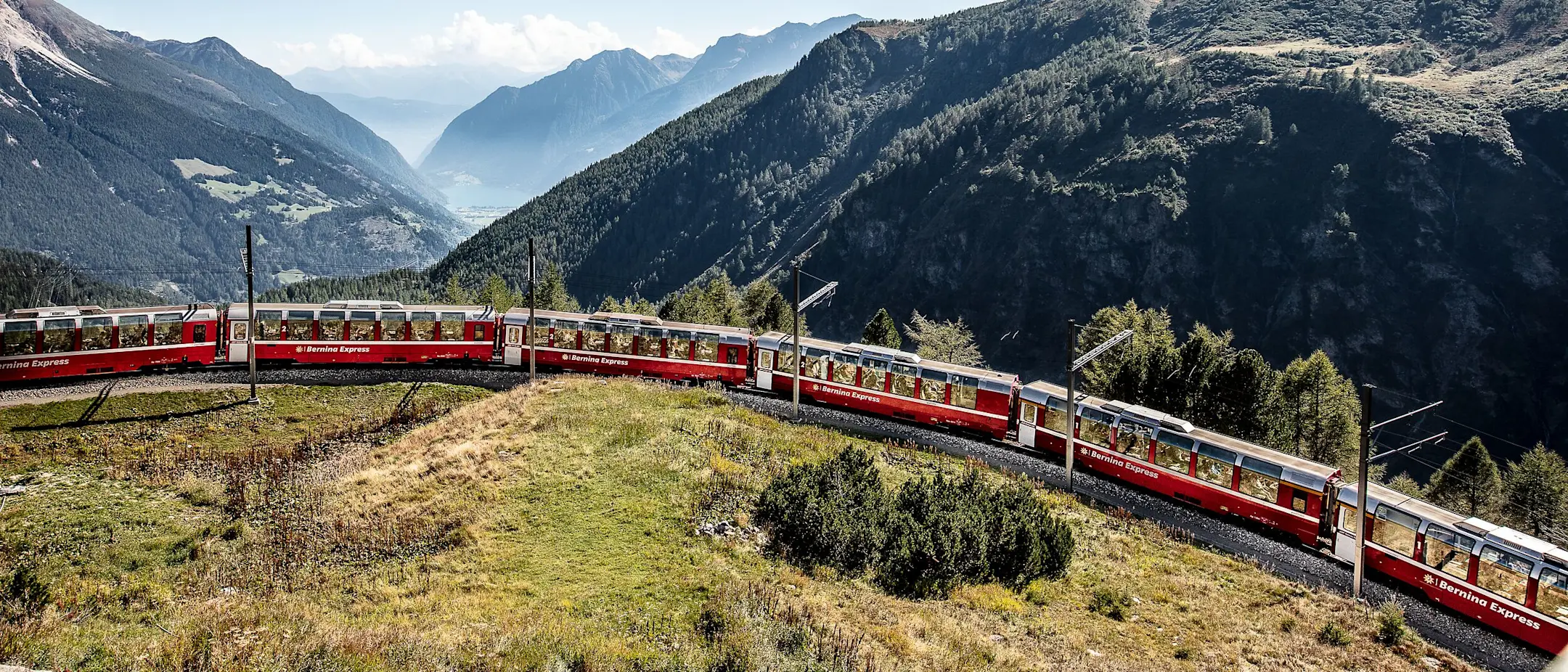 Der Bernina Express fährt bei der Alp Grüm eine Kurve. Im Hintergrund sieht man ins Tal Richtung Val Poschiavo.