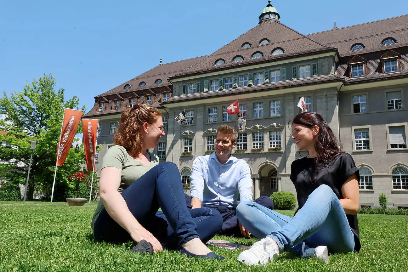 Drei Mitarbeitende auf dem Rasen vor der RhB-Verwaltung in Chur.