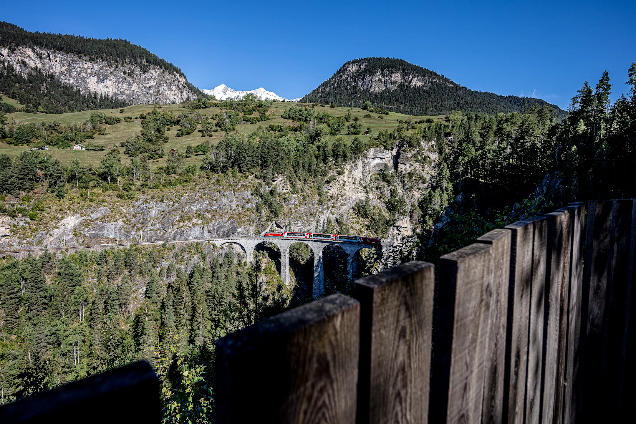 Die Aussichtsplattform Acatos mit Blick auf einen vorbeifahrenden Zug und das Landwasserviadukt