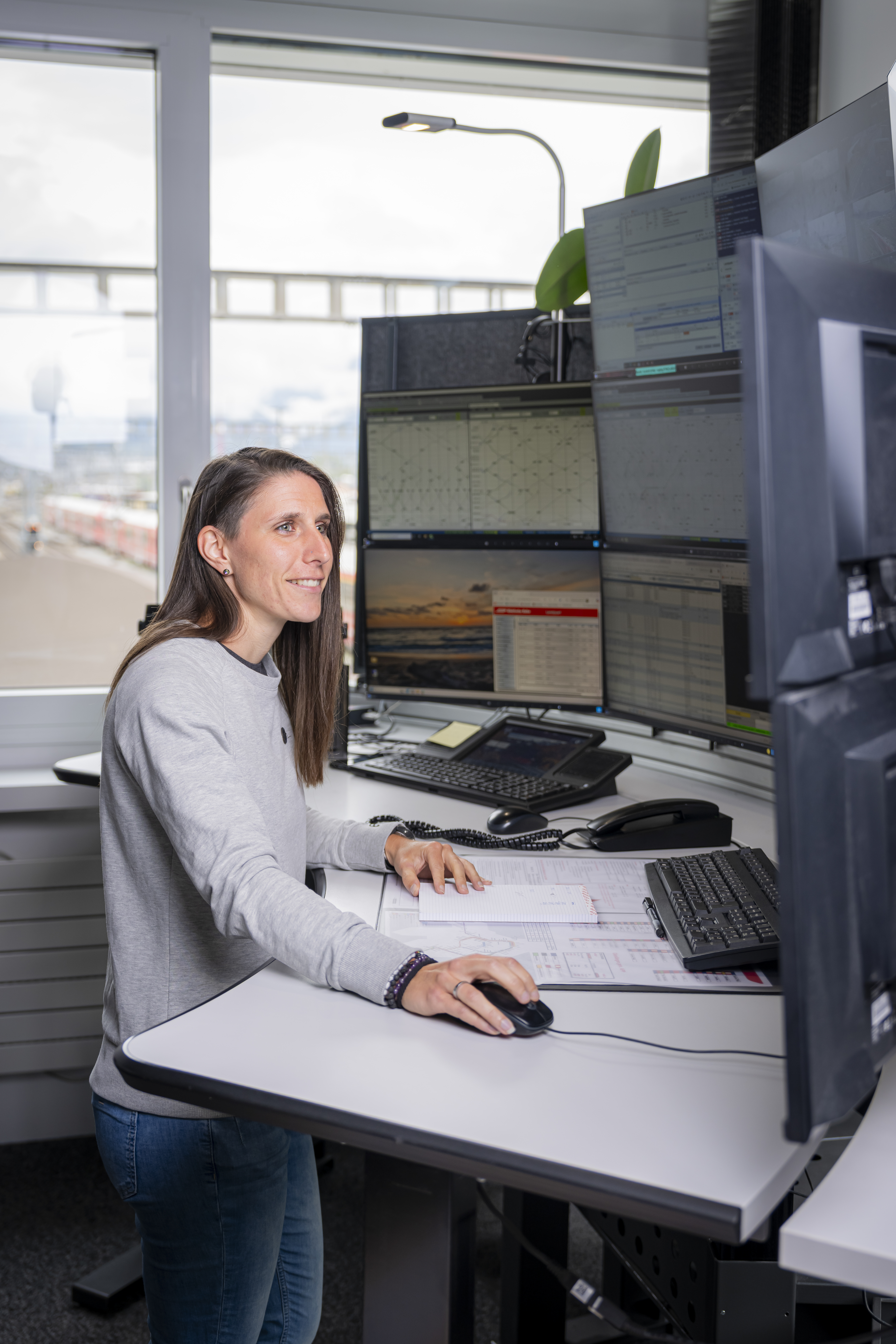 A RhB train dispatcher stands at her desk in front of numerous monitors.