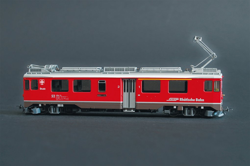 Detailliertes Modell eines roten Zuges der Rhätischen Bahn mit der Aufschrift „Brusio“, vor neutralem grauen Hintergrund.