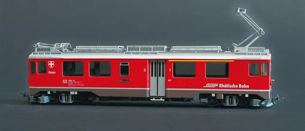 Detailliertes Modell eines roten Zuges der Rhätischen Bahn mit der Aufschrift „Brusio“, vor neutralem grauen Hintergrund.