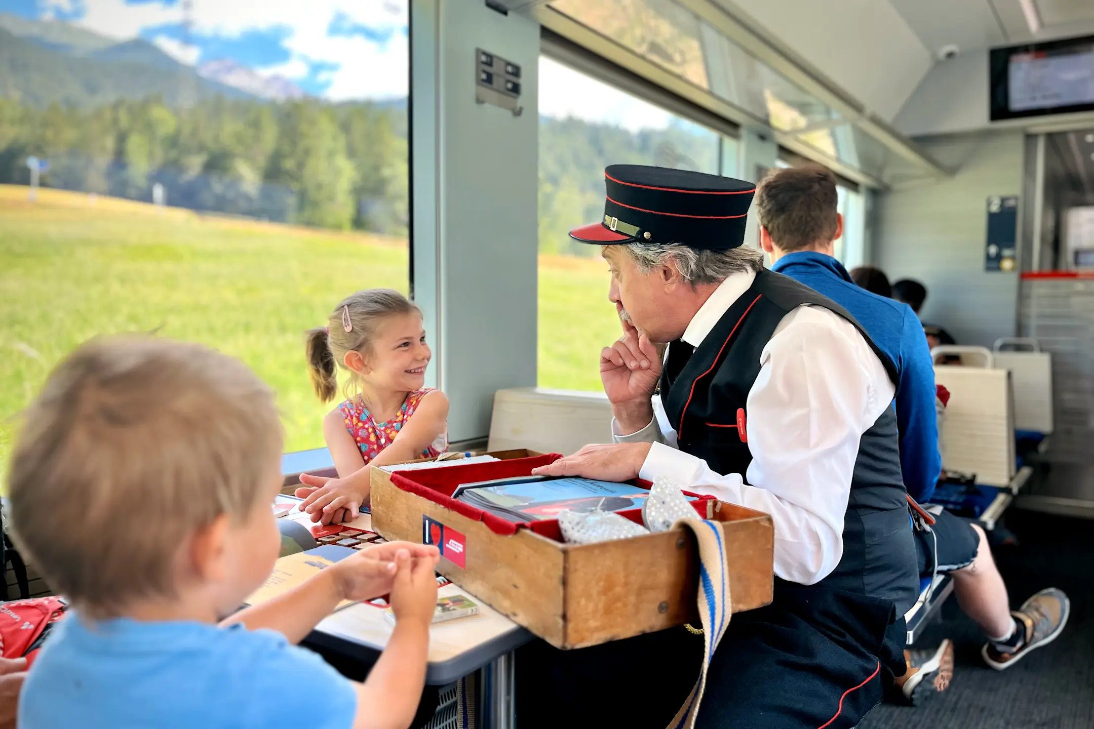Der Kinderkondukteur Clà Ferrovia der Rhätischen Bahn spielt mit einem Kind im Familienabteil