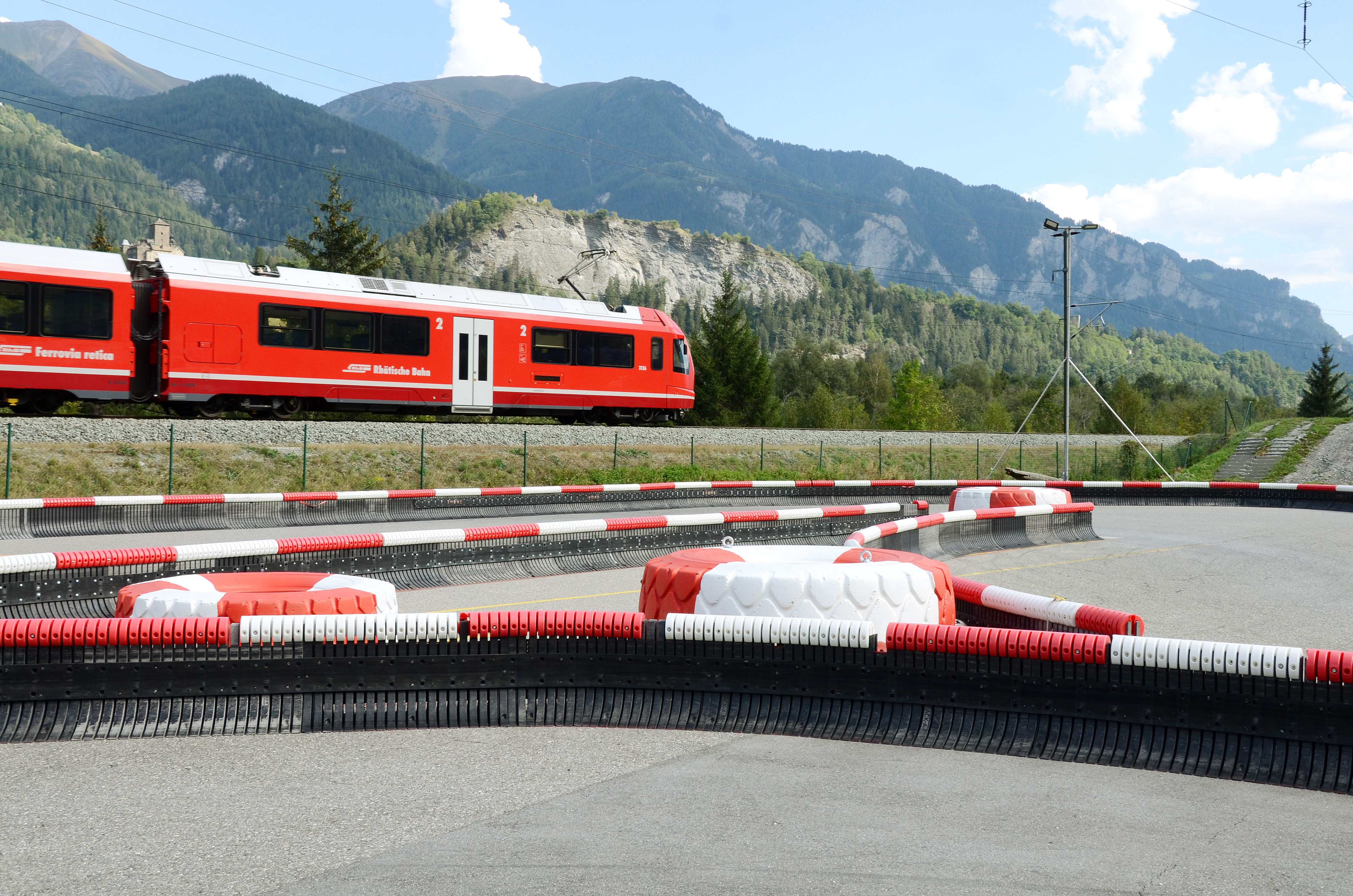 Ein roter RhB-Zug fährt entlang der Rennbahn von Outdoorkart Graubünden. 