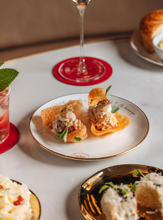 Elegant appetizers on a white plate adorned with gold leaf, accompanied by a glass of champagne