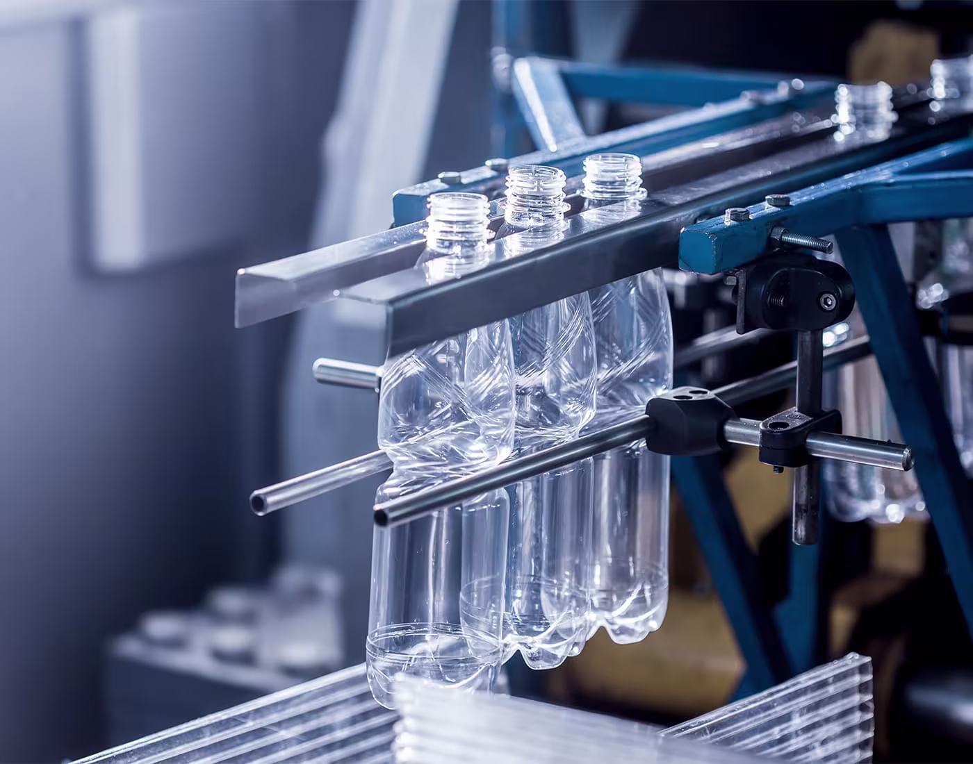 Mehrere transparente Kunststoffflaschen hängen kopfüber in einer industriellen Produktionsanlage aus Metallgestänge.