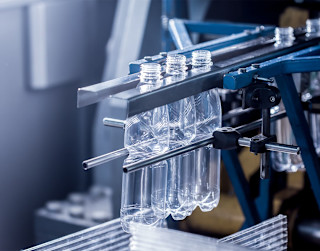 Mehrere transparente Kunststoffflaschen hängen kopfüber in einer industriellen Produktionsanlage aus Metallgestänge.