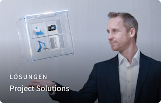 Ein Mann in Businesskleidung präsentiert ein schwebendes, transparentes Würfelmodell mit technischen Komponenten, daneben steht der Text „Lösungen – Project Solutions“.