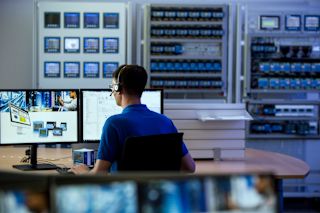 Técnico con auriculares trabajando en un escritorio con monitores en un entorno lleno de dispositivos de monitoreo de energía