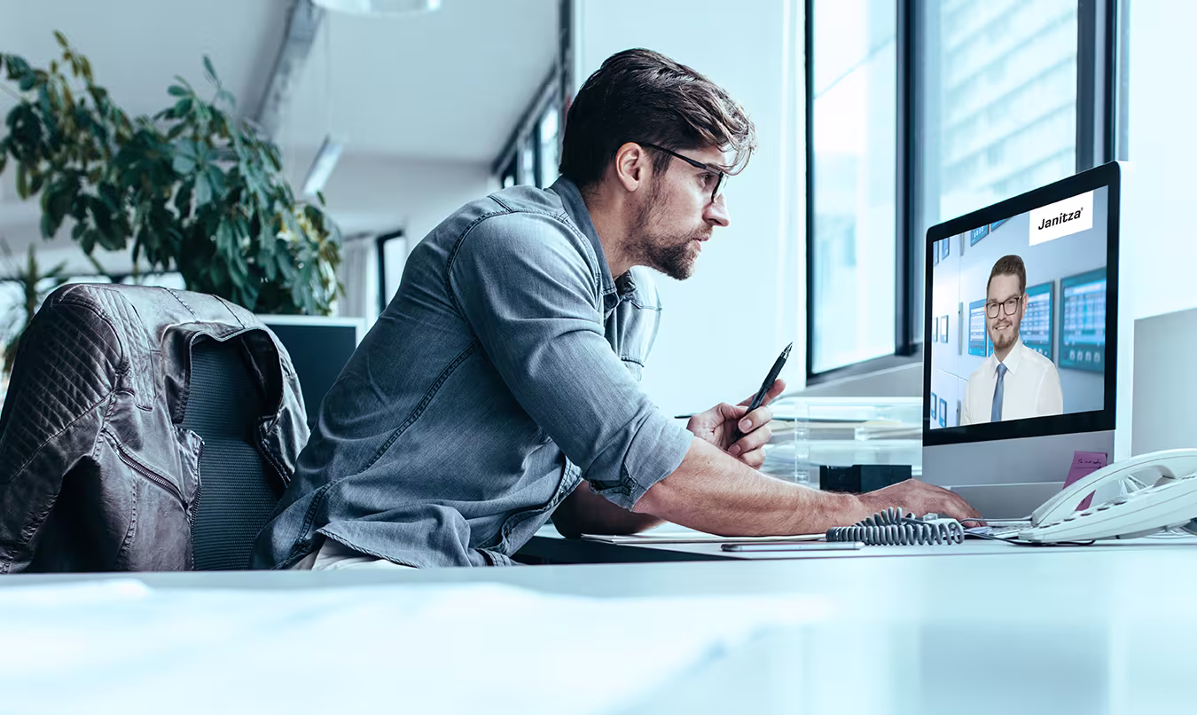 Young man working intently at a desk with a laptop showing a video conference
