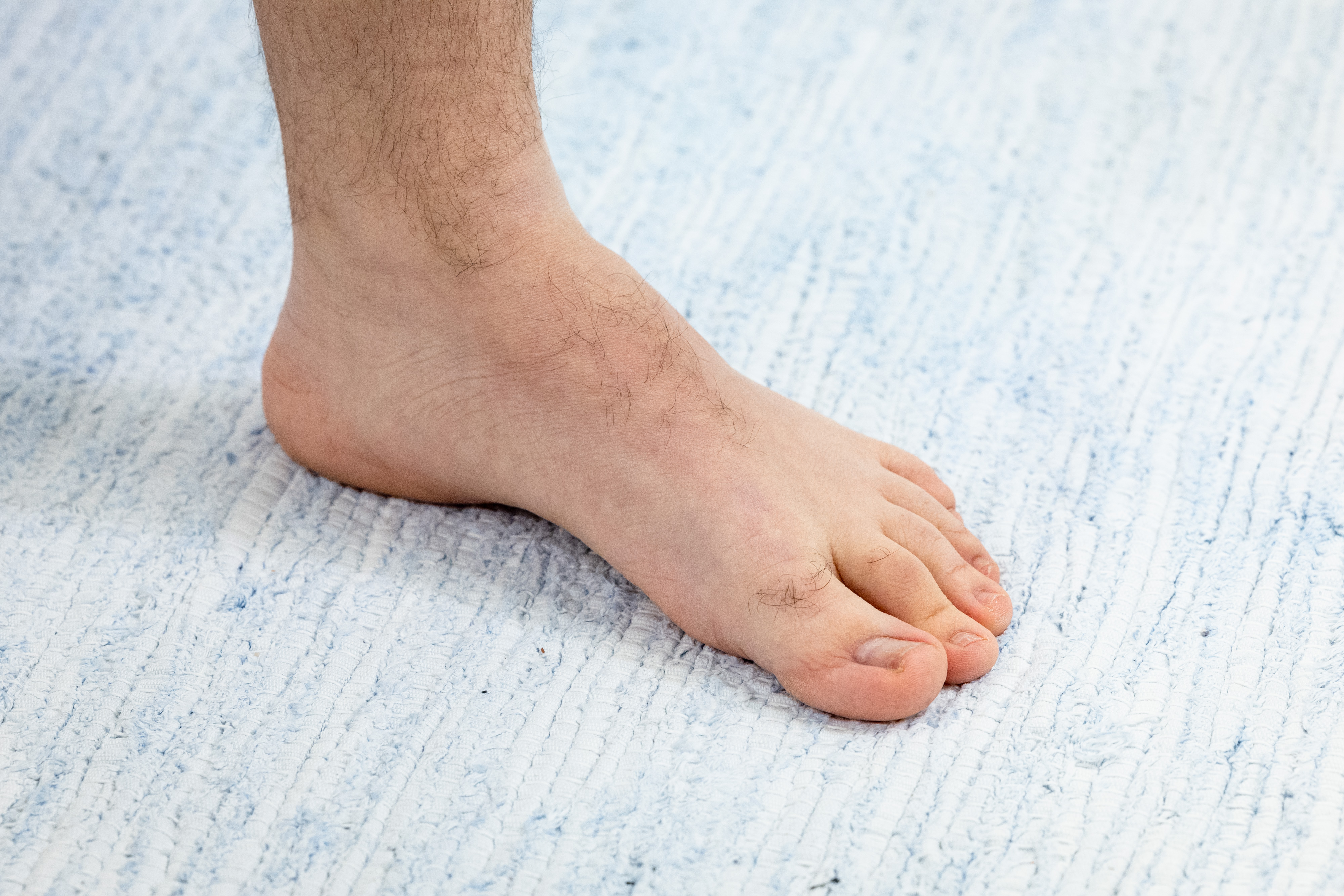 Miehen paljas jalkapohja on lattialla maton päällä. 