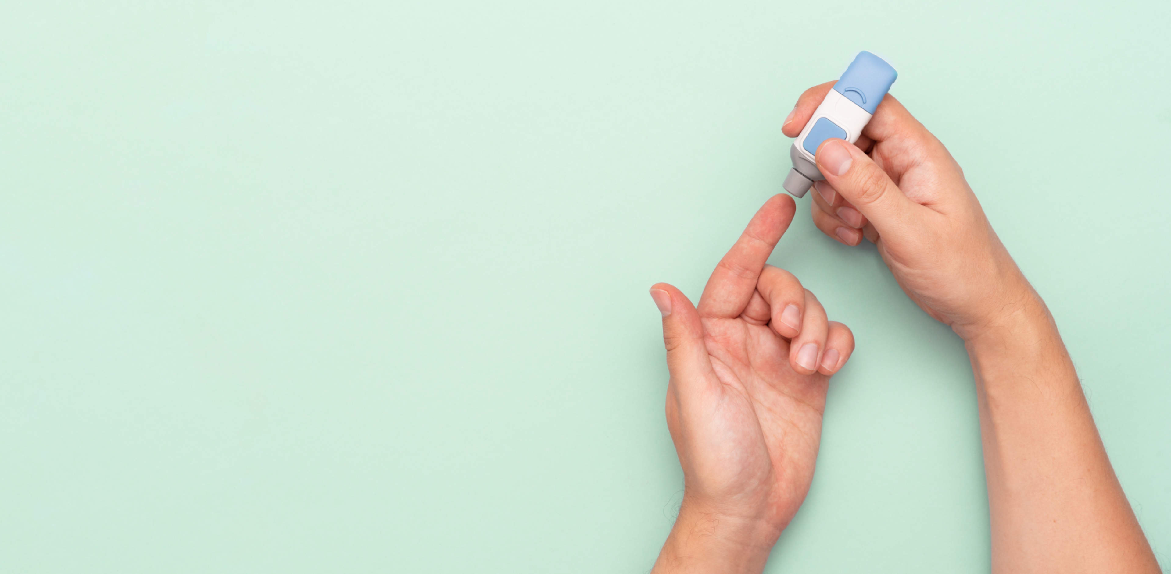In the image, a lancet pen held in the right hand is about to be used to make a prick in the left hand's index finger.