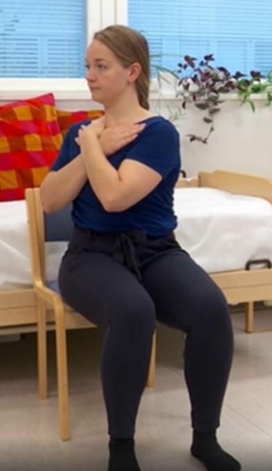 Nainen istuu kädet ristissä rinnalla ja kiertää rintakehän oikealle puolelle.