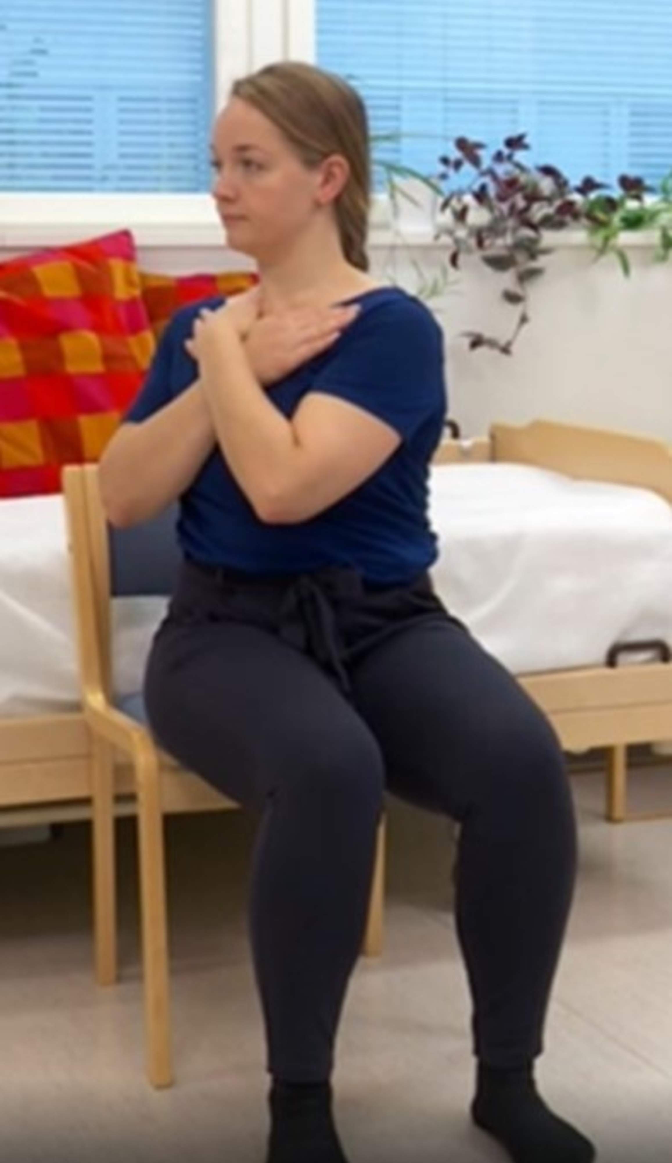 En kvinna sitter med armarna korsade över bröstet och vrider bröstkorgen åt höger.