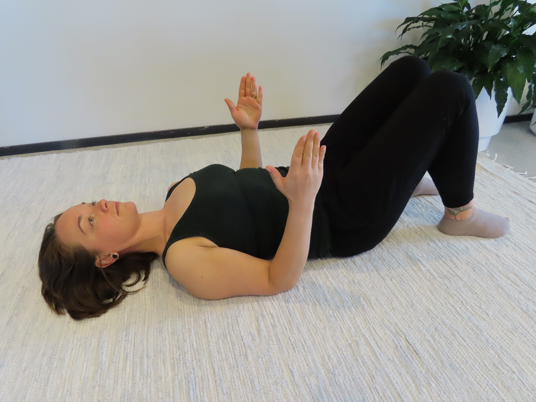 Nainen makaa selinmakuulla lattialla, polvet koukussa, kädet vartalon vierellä, kyynärpäät koukistettuina ja sormet kohti kattoa.