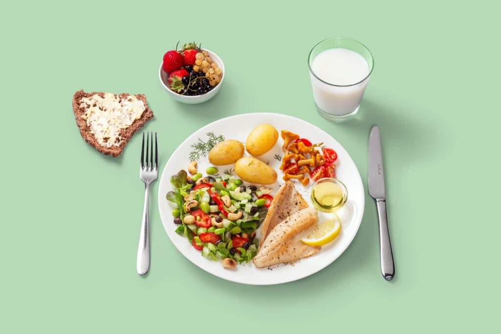 Ett exempel på en lunchmåltid. En tallrik med stekt fisk, potatis och sallad, en bit rågbröd, ett glas mjölk och en dessertskål med bär.