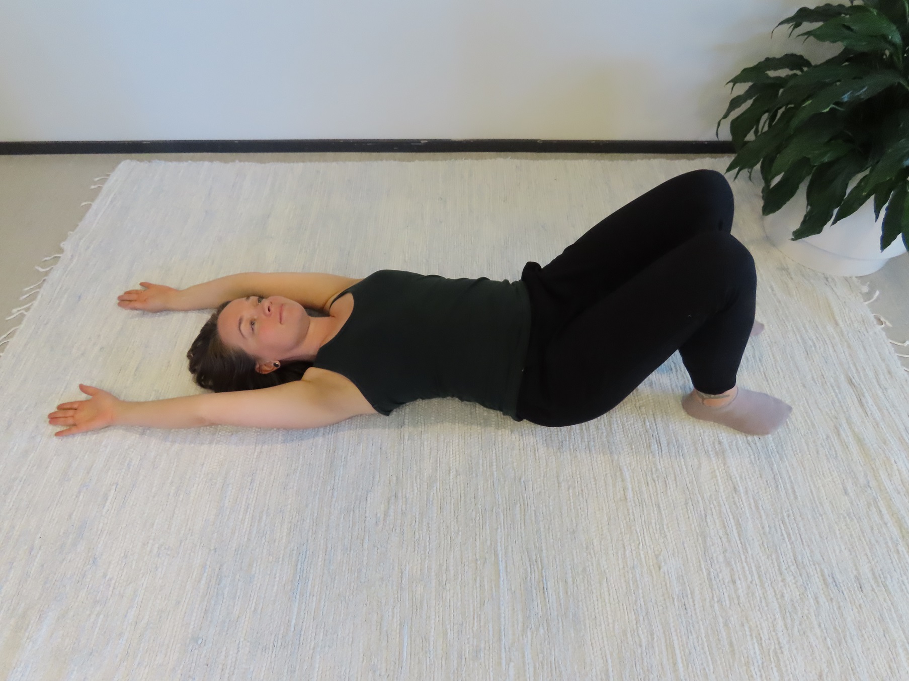 Nainen makaa selinmakuulla lattialla, polvet koukussa ja kädet vietynä lattiaa pitkin sivulta pään vierelle kämmenselät lattiaa vasten. 