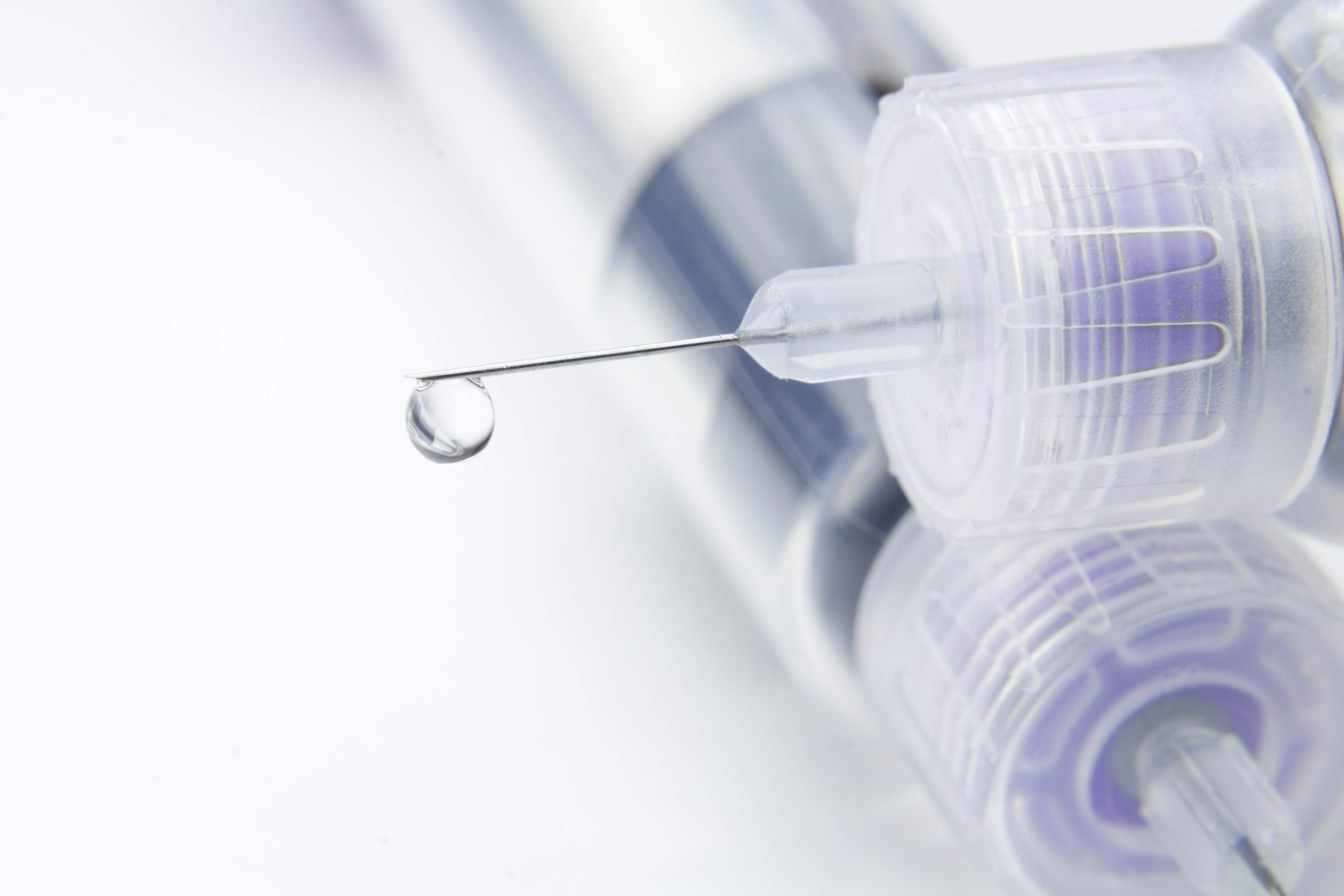 In the picture, there is a needle attached to an insulin pen, with a drop of insulin visible at the tip.