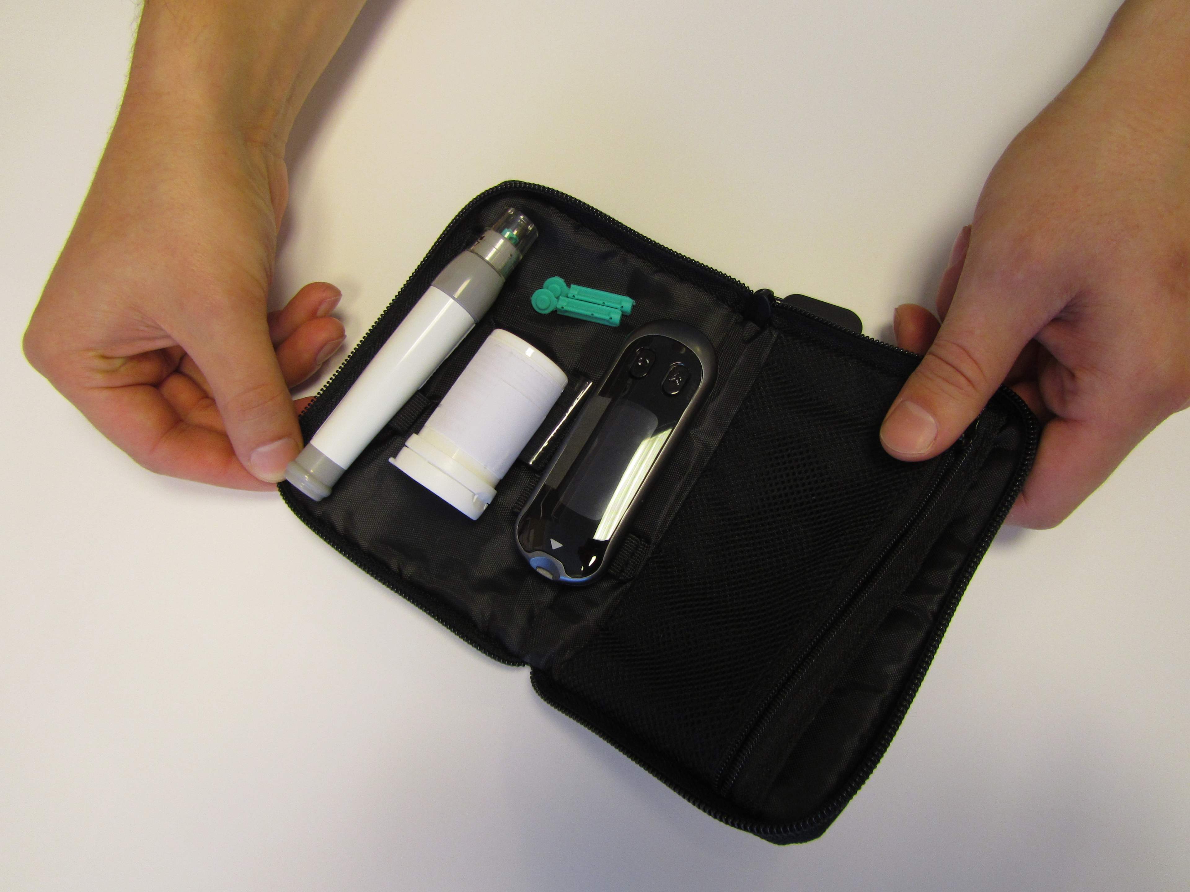 In the image is a blood glucose meter, a strip container, a lancet pen, and lancet needles in their own storage case.