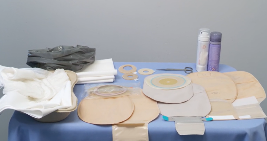 Pöydällä on avannesidos tarvikkeita: yksi- ja kaksiosaisia avannepusseja, avannepussin pohjalevy, liiman irrotussuihkeita, pastarenkaita, sakset, roskapussi, kosteita ja kuivia paperipyyhkeitä.